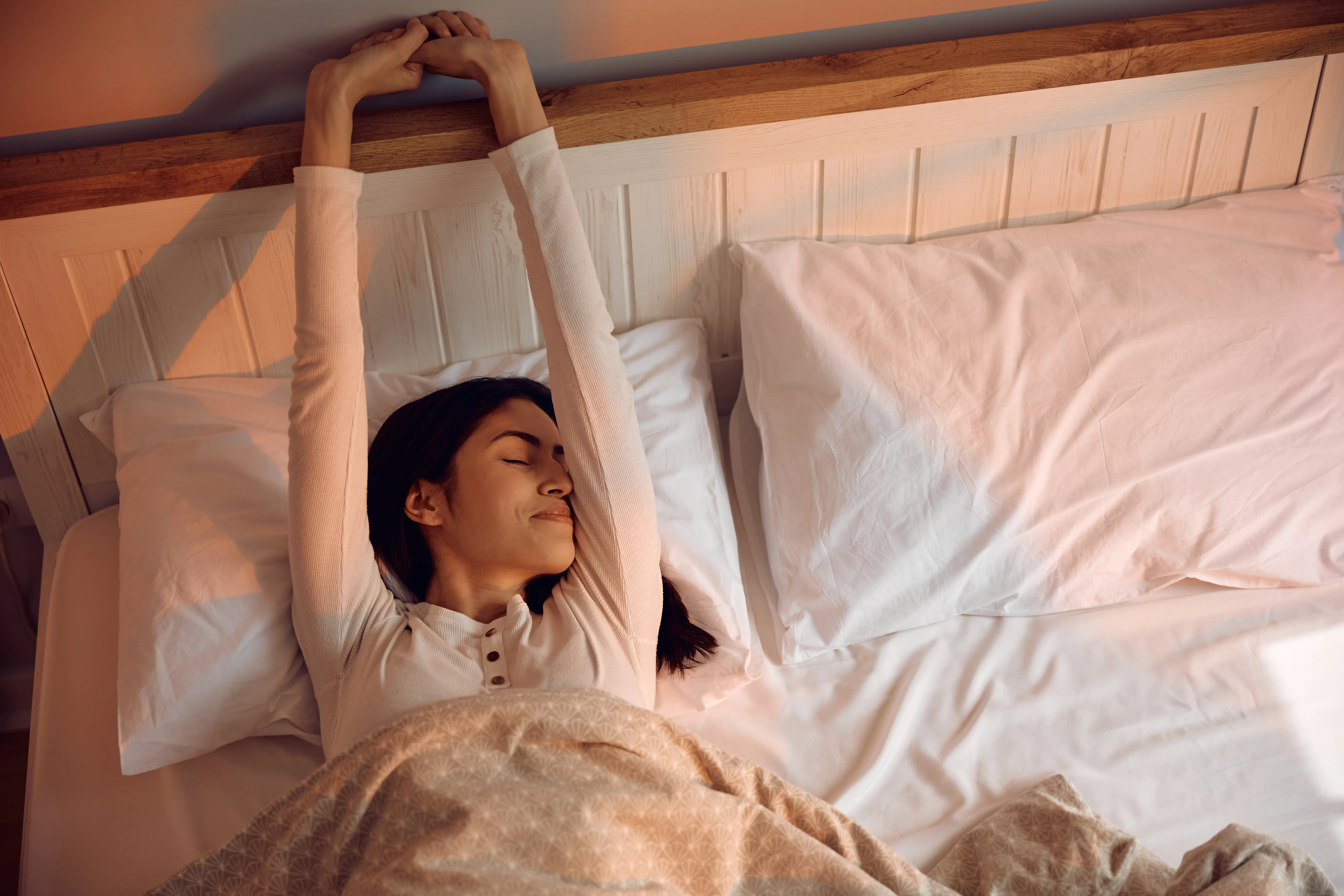 Above view of smiling woman waking up in bedroom.