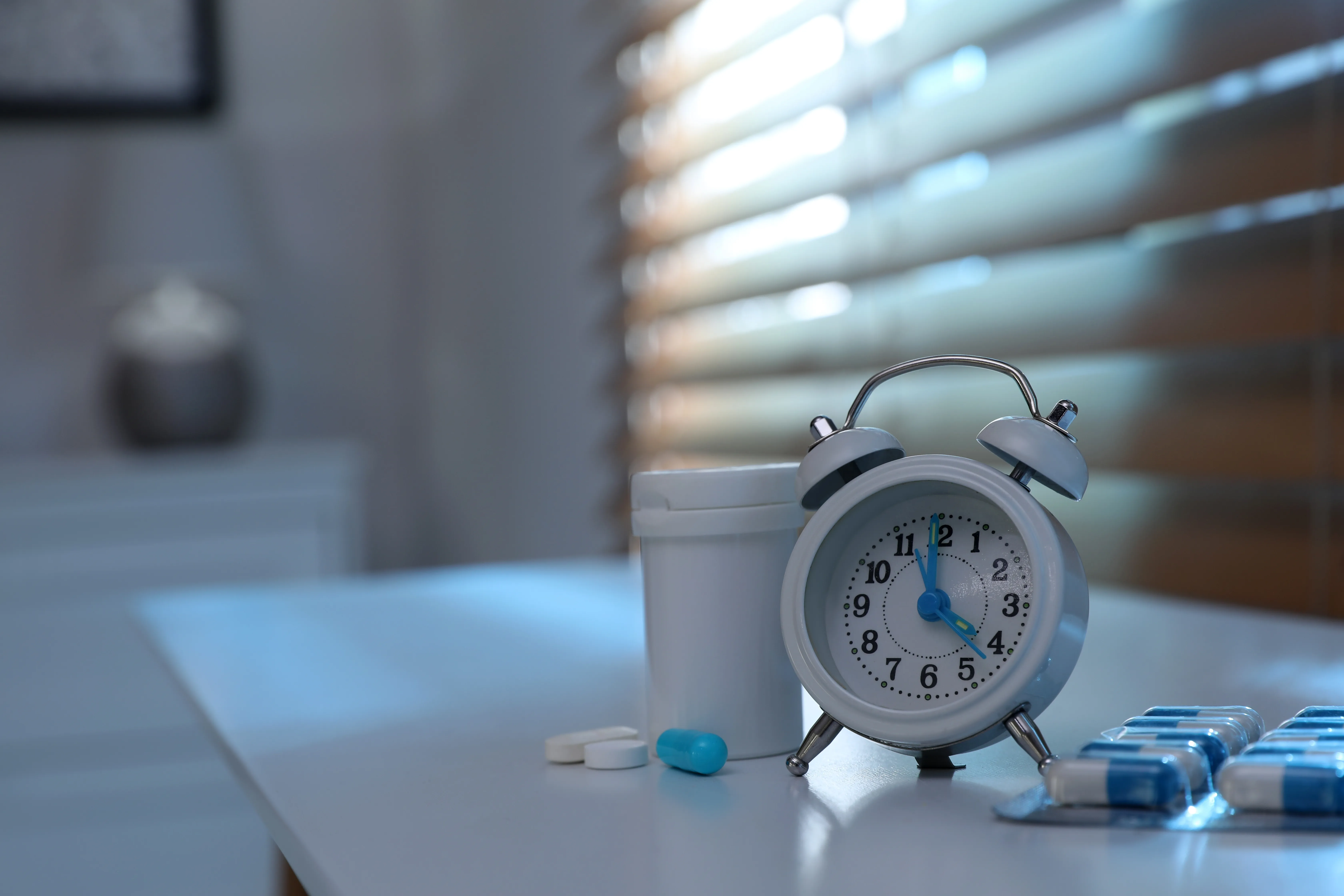 sleep medication beside a glass of water and an alarm clock