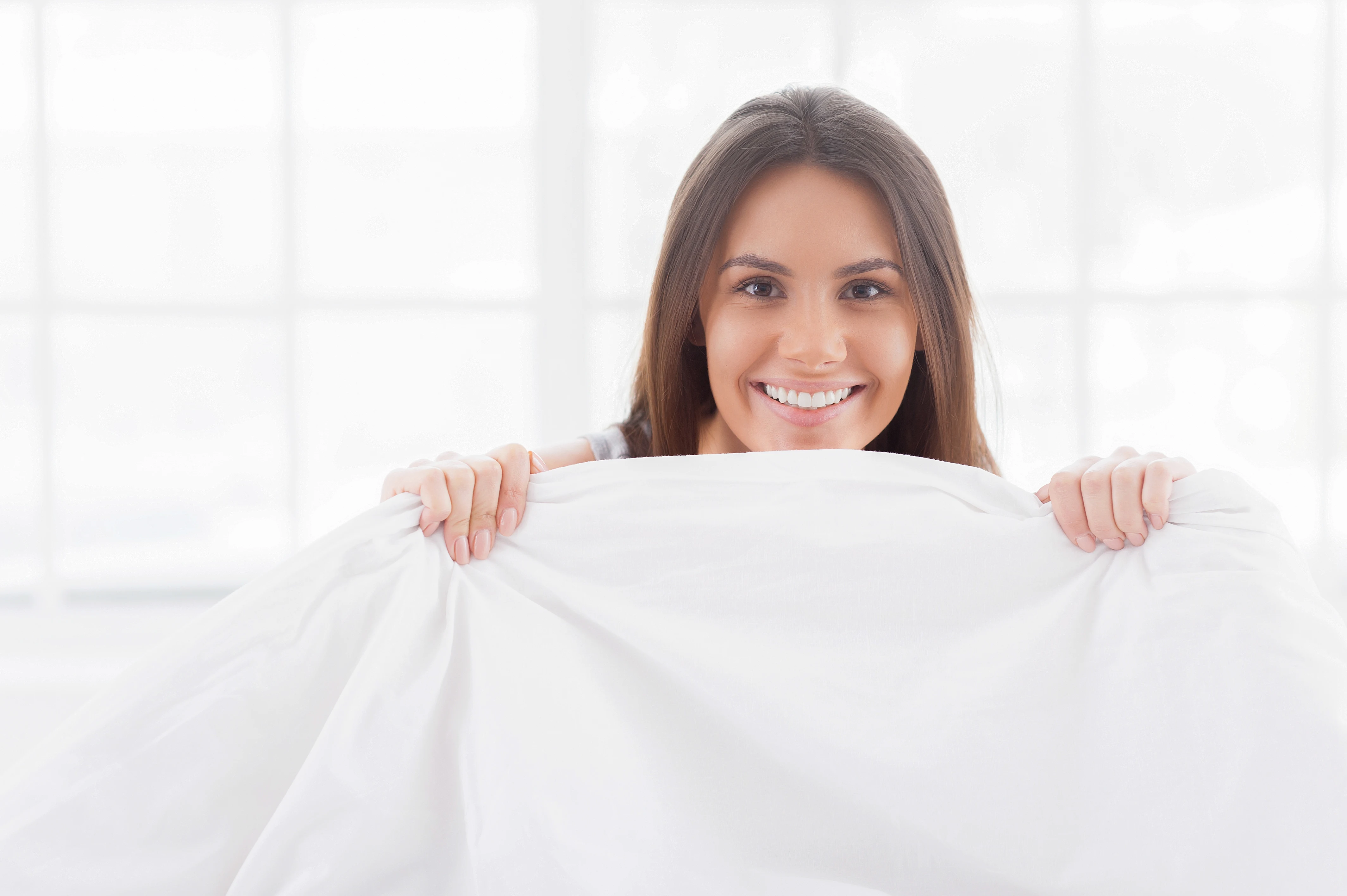 Person sitting beneath clean white bed sheets
