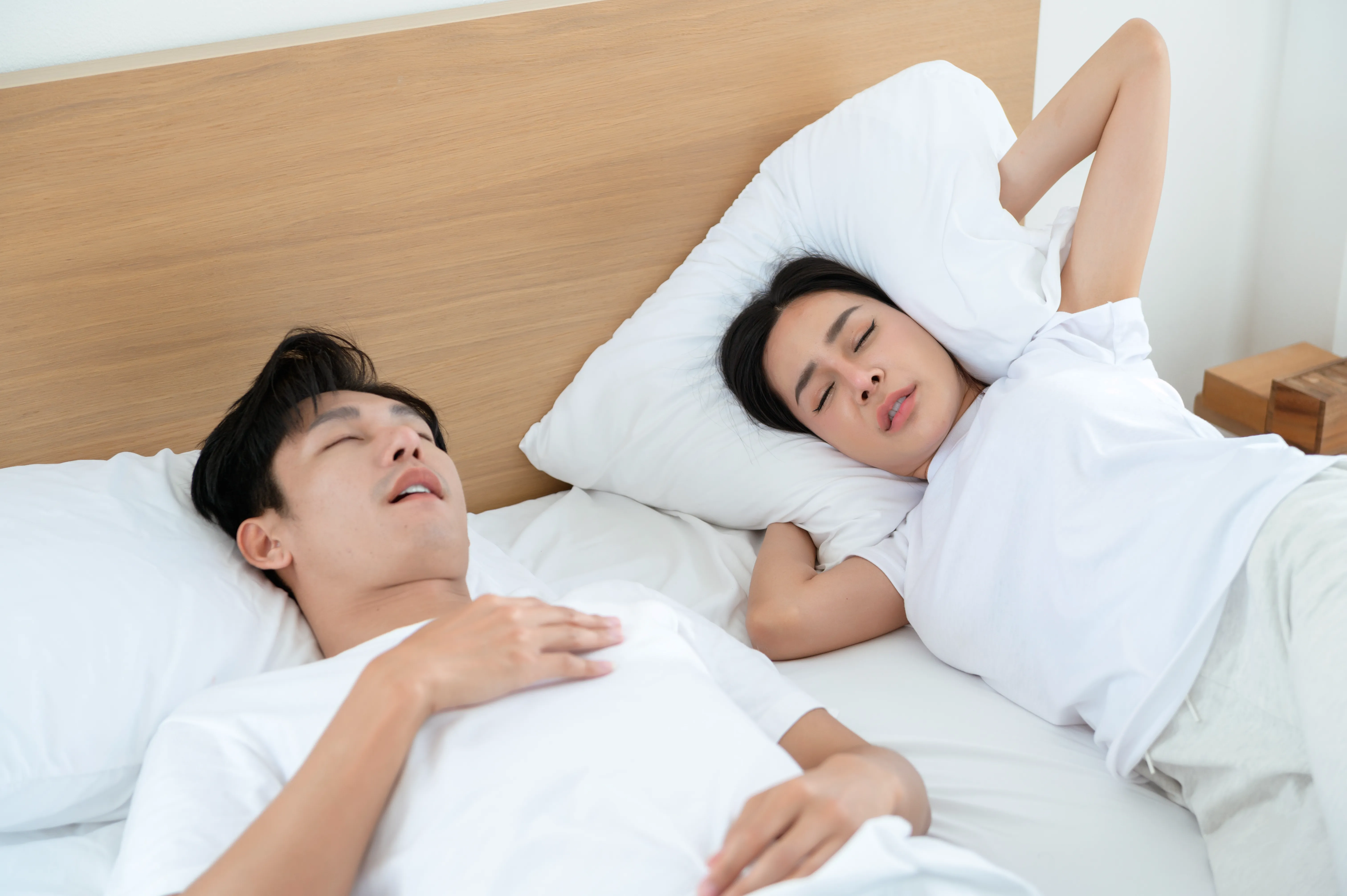Couple Sleeping in Bed With One Partner Snoring Loudly in a Bright Room