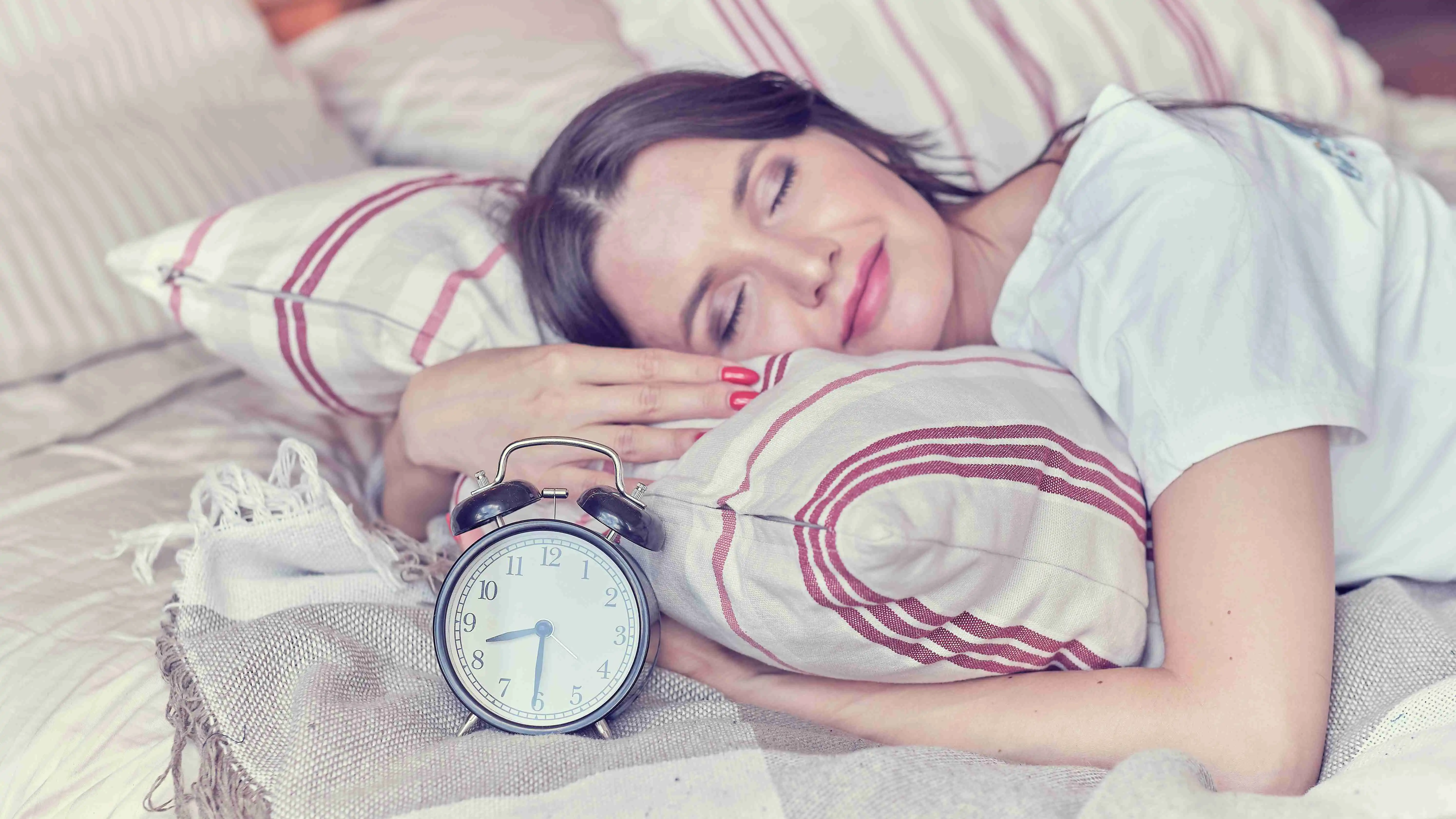 Young sleeping woman and alarm clock in bedroom at home