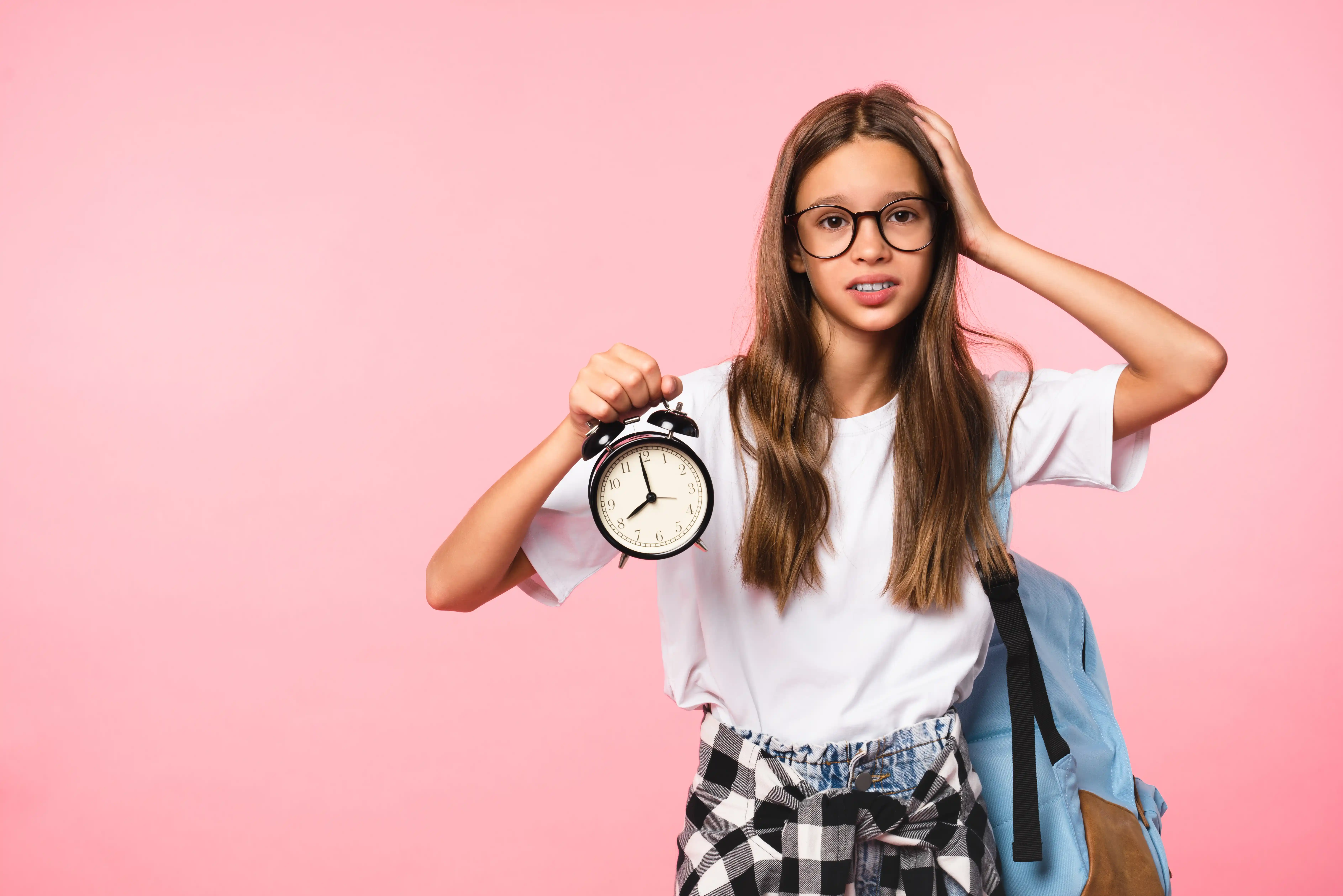 Scared schoolgirl hurrying up to school with clock in hands. Time back to school!