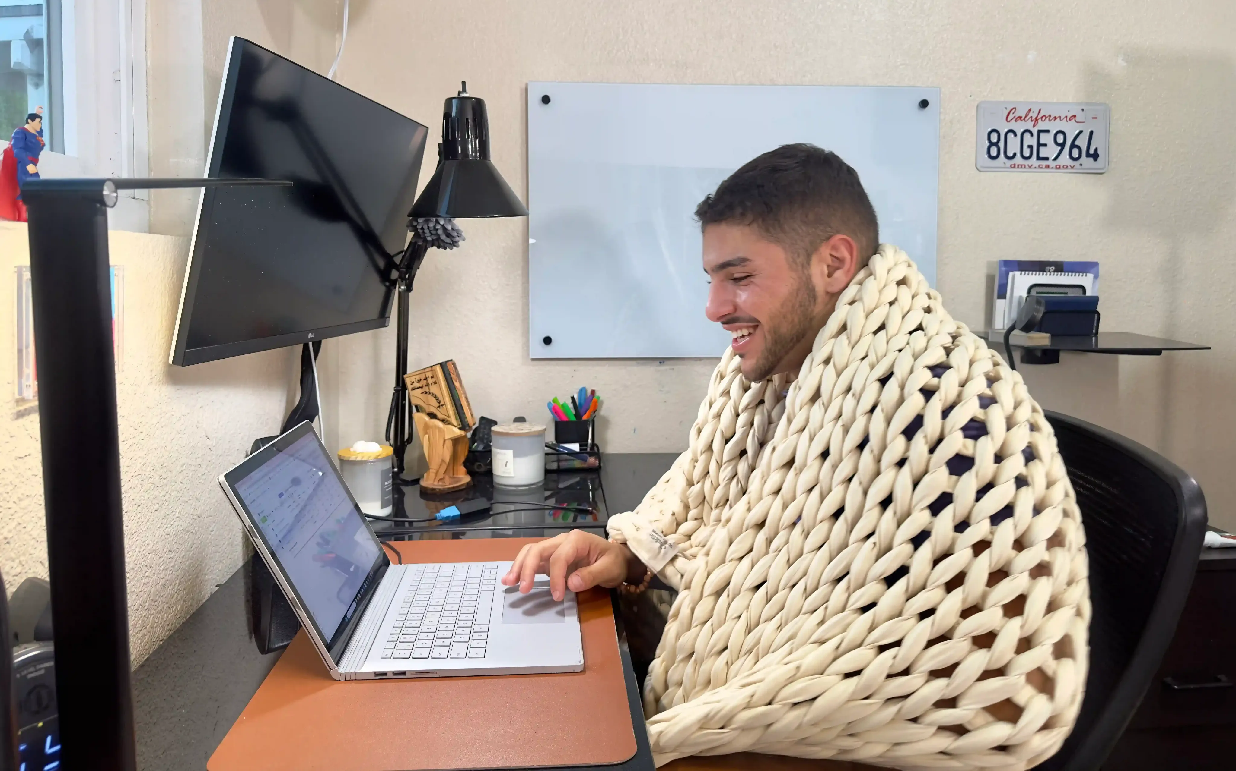 Reviewer from Sleepiverse Studio sitting on a chair, working on a laptop, with the Cuddler weighted blanket draped over them
