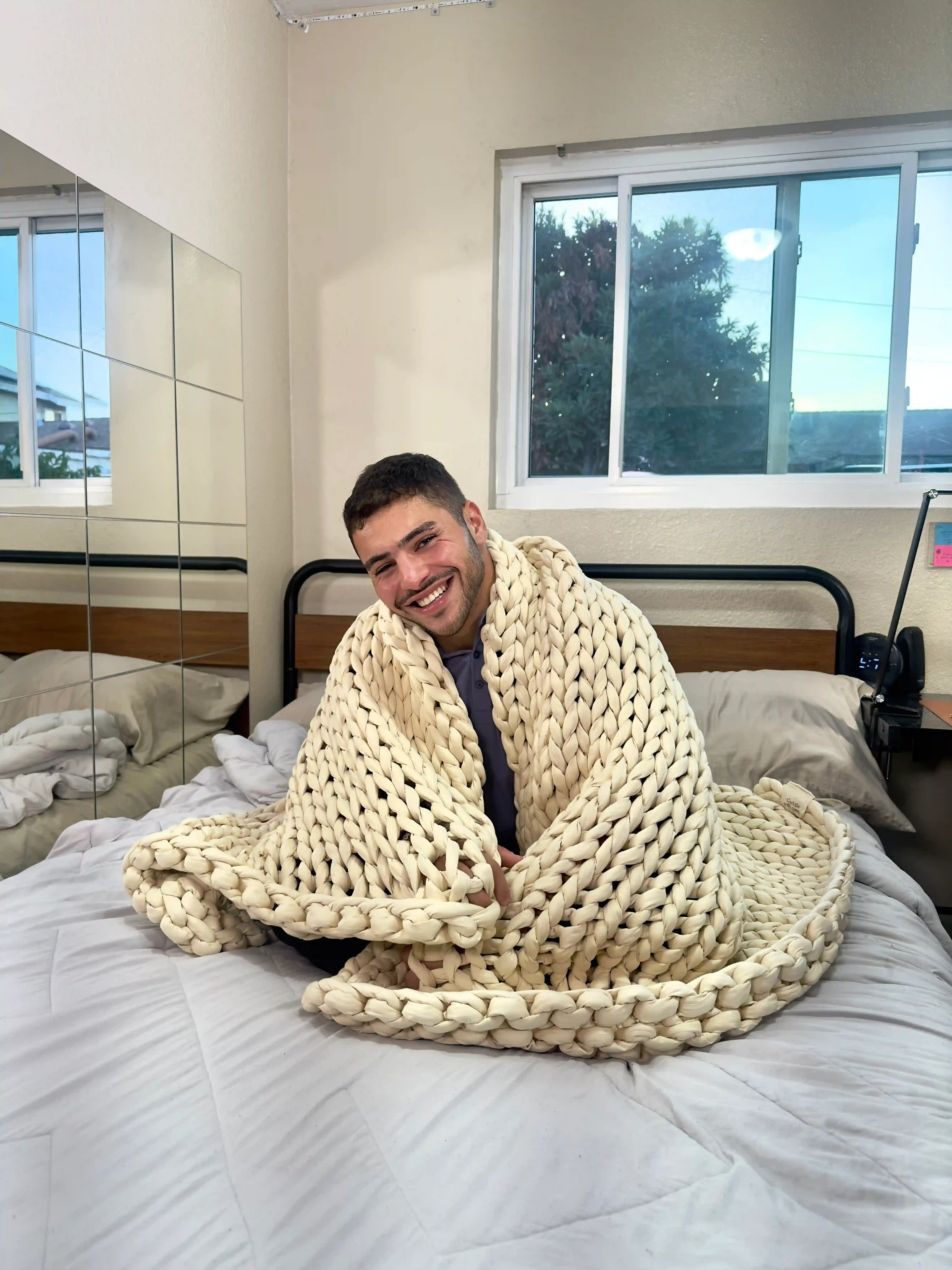 Reviewer from Sleepiverse Studio sitting on a mattress with the Cuddler weighted blanket draped over them