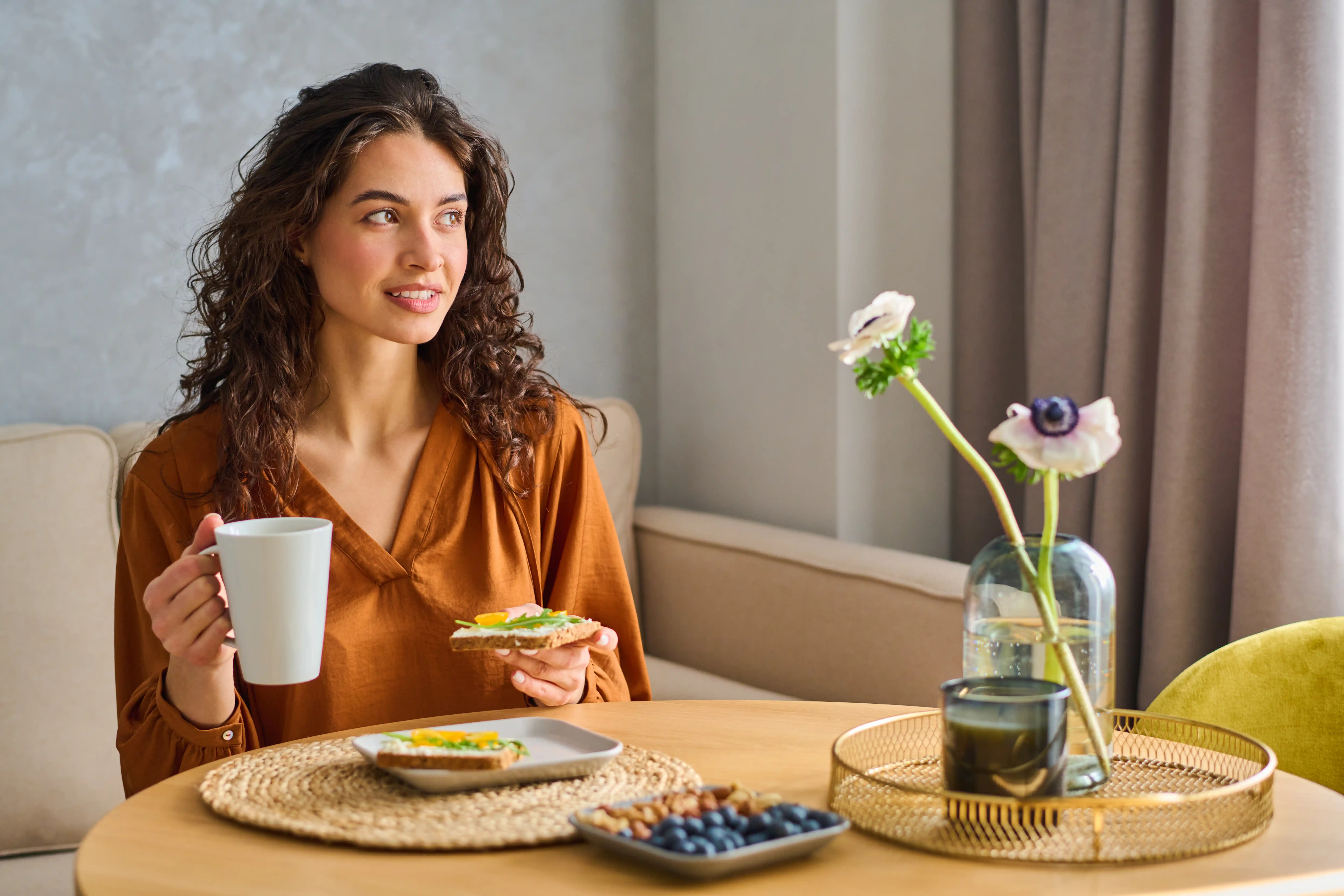 Happy young female vegetarian in casual blouse having tea with sandwich