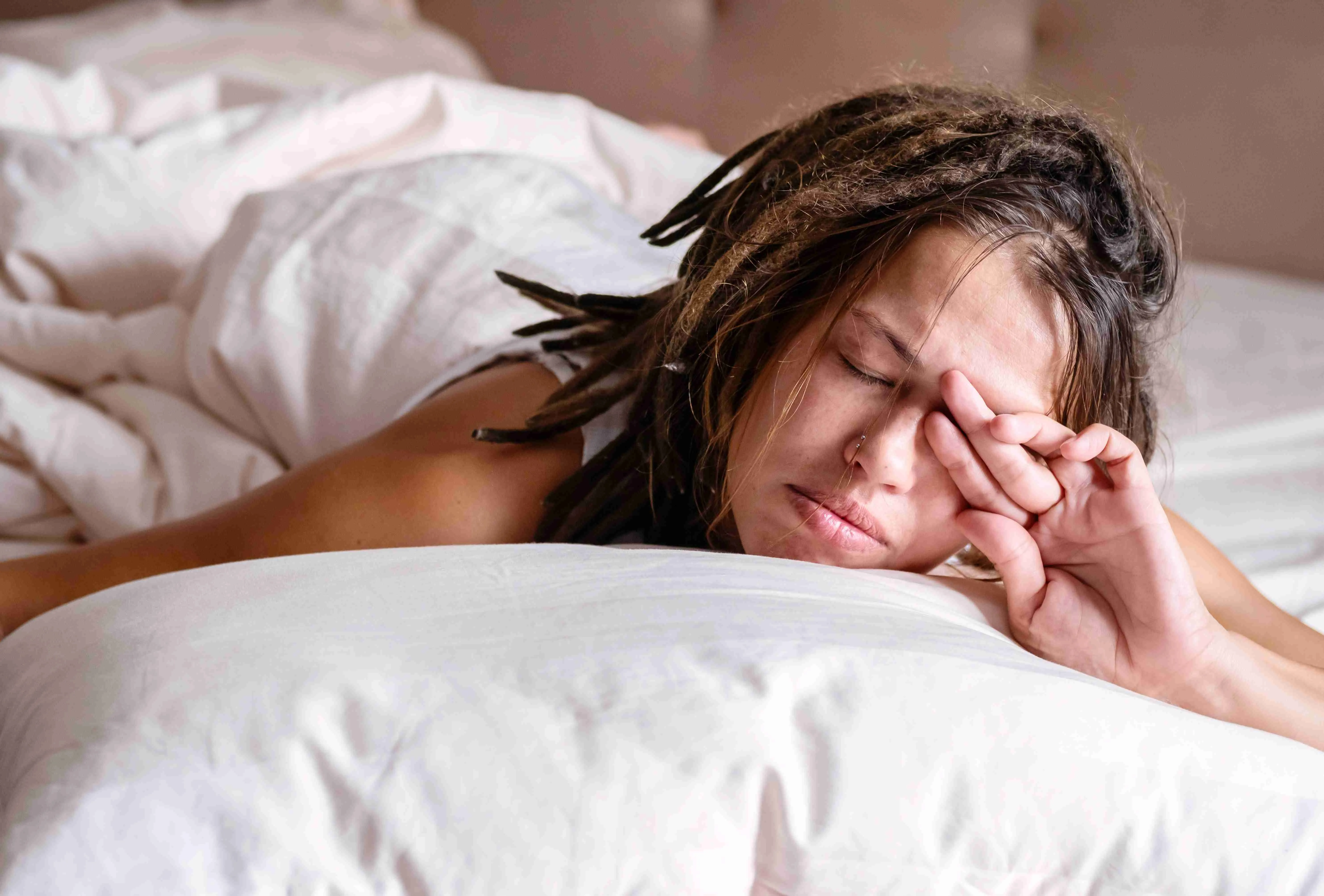 Woman covering his eyes from the morning light in the bed.