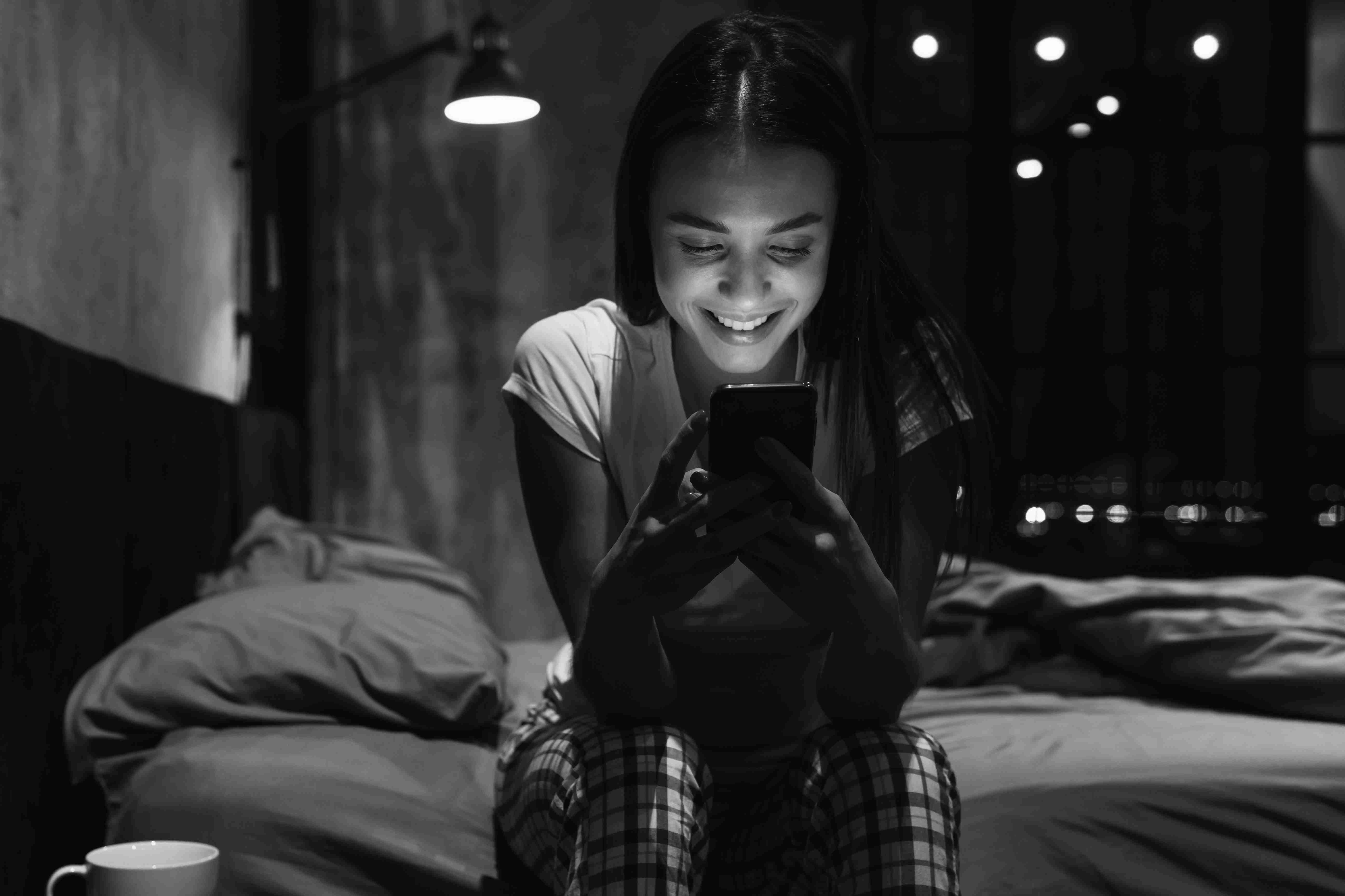 Beautiful attractive woman sits alone in bedroom at night chatting using smartphone