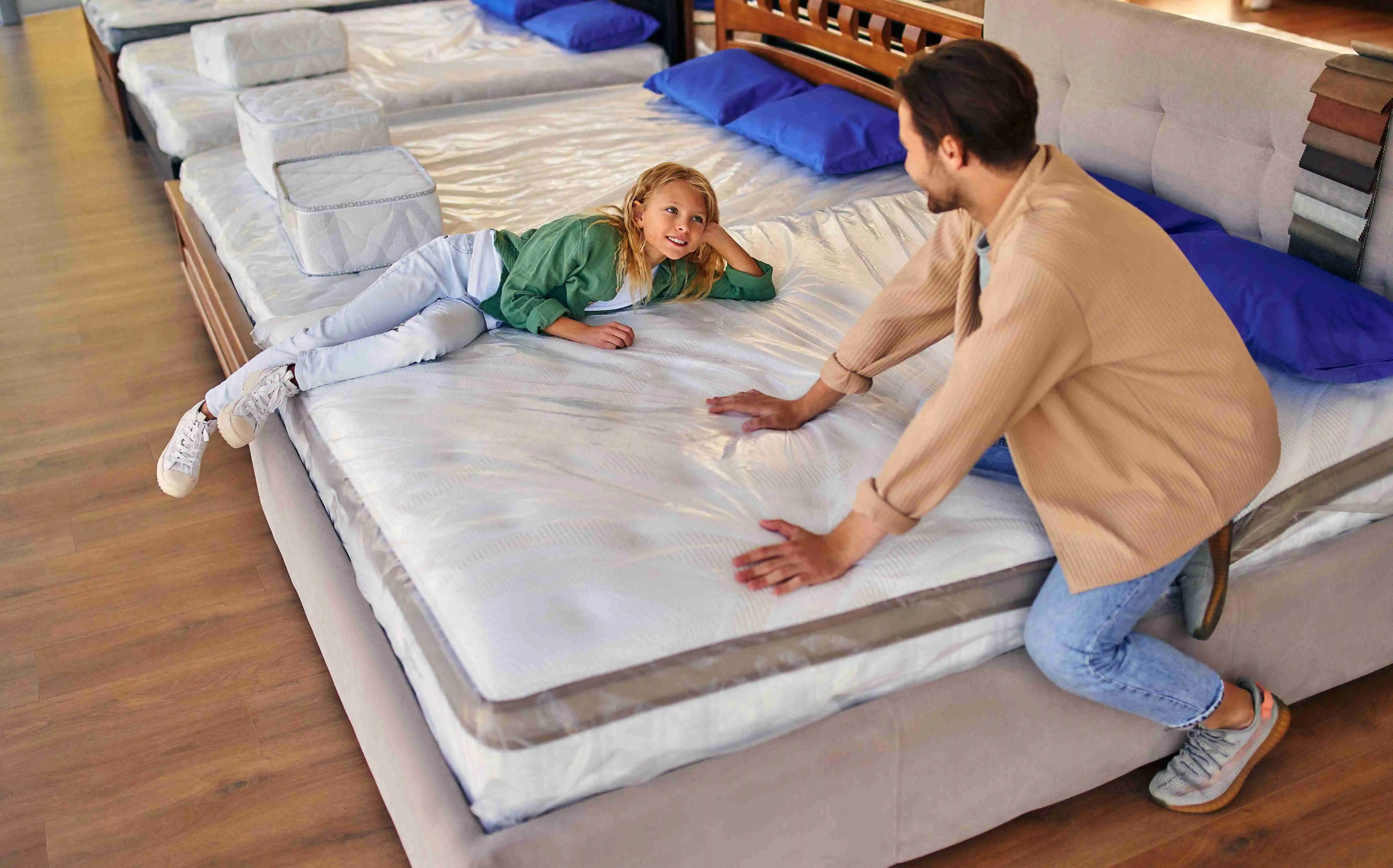 A young man, dad, with his lovely daughter lay down on the bed, trying the mattress for softness in the store.