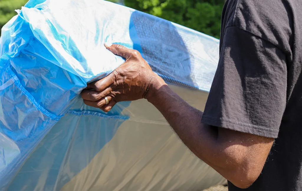 A person is moving a blue plastic-covered mattress outdoors.