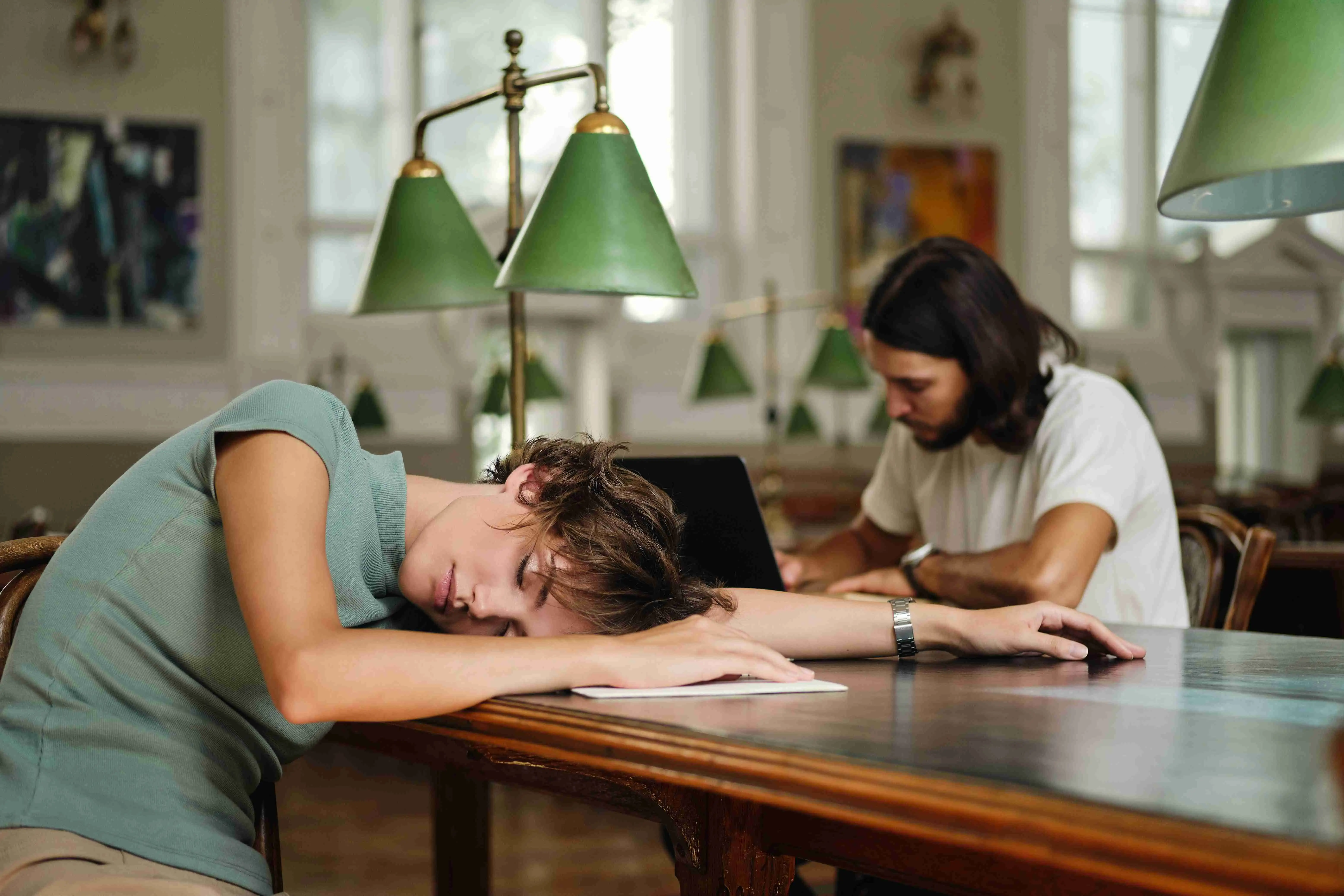 Young tired female student sleeping on desk during study in library of university