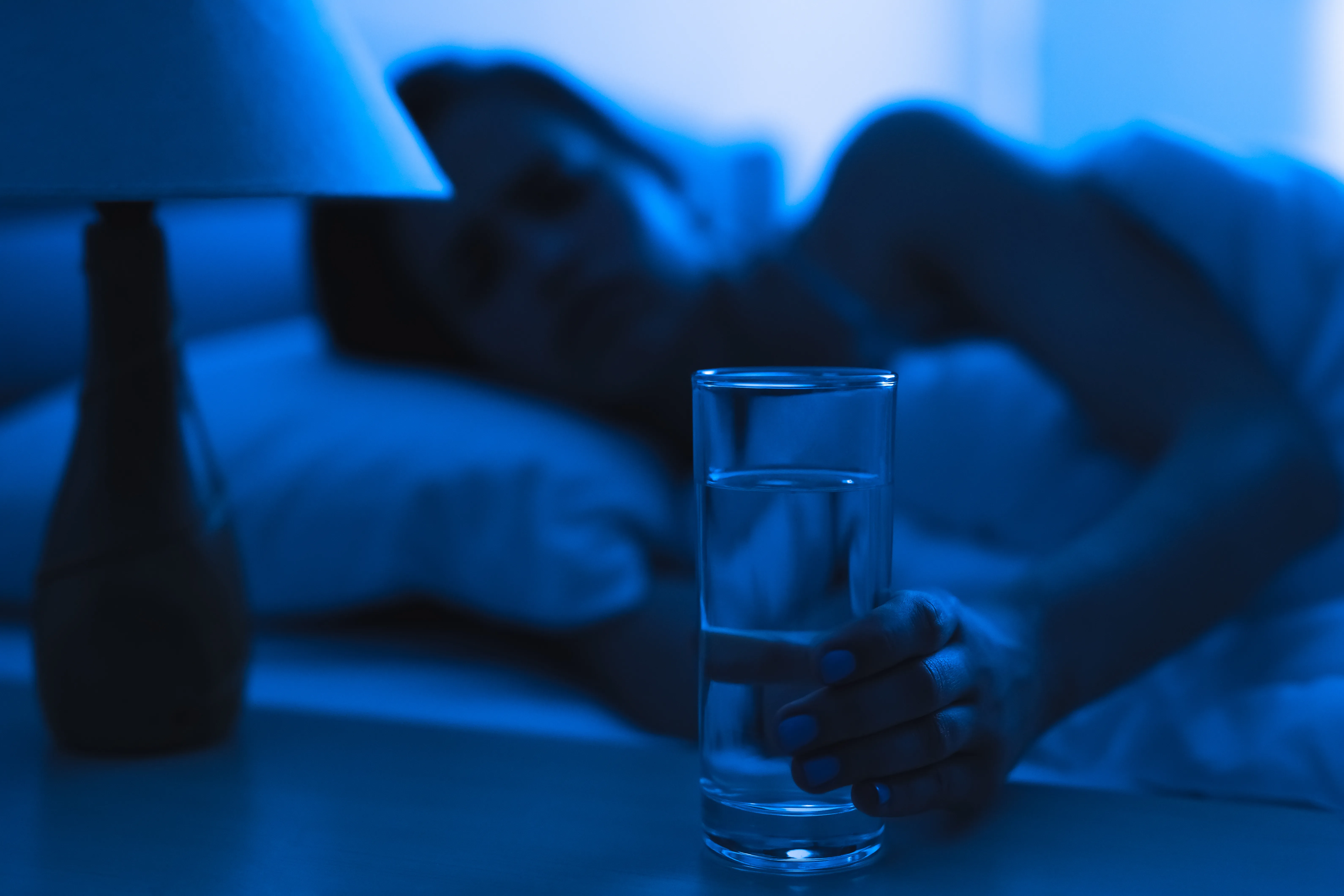 The woman on the bed holding a cup of water. evening night time