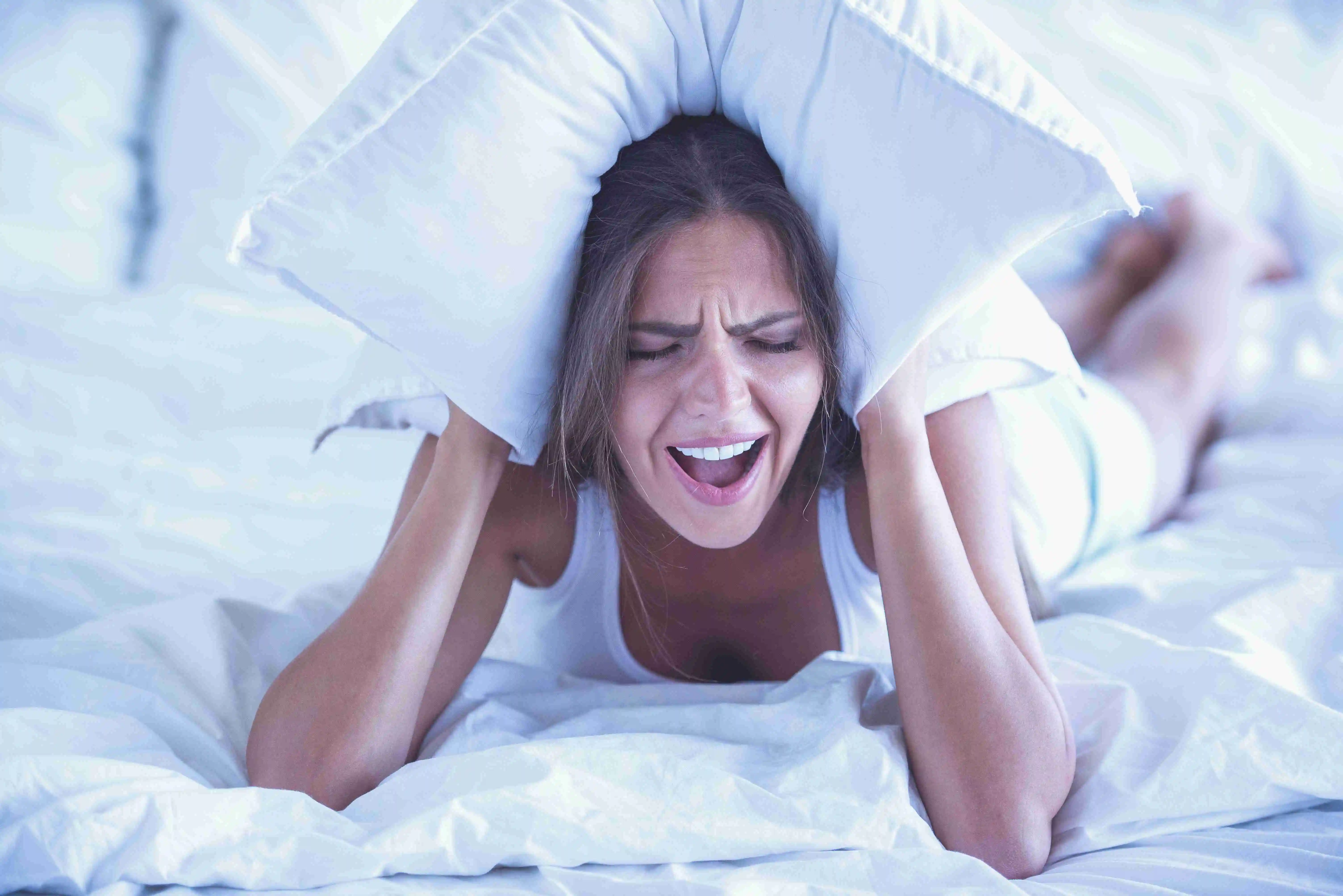 Person lying on bed, covering ears with a pillow, and screaming, indicating frustration or distress.