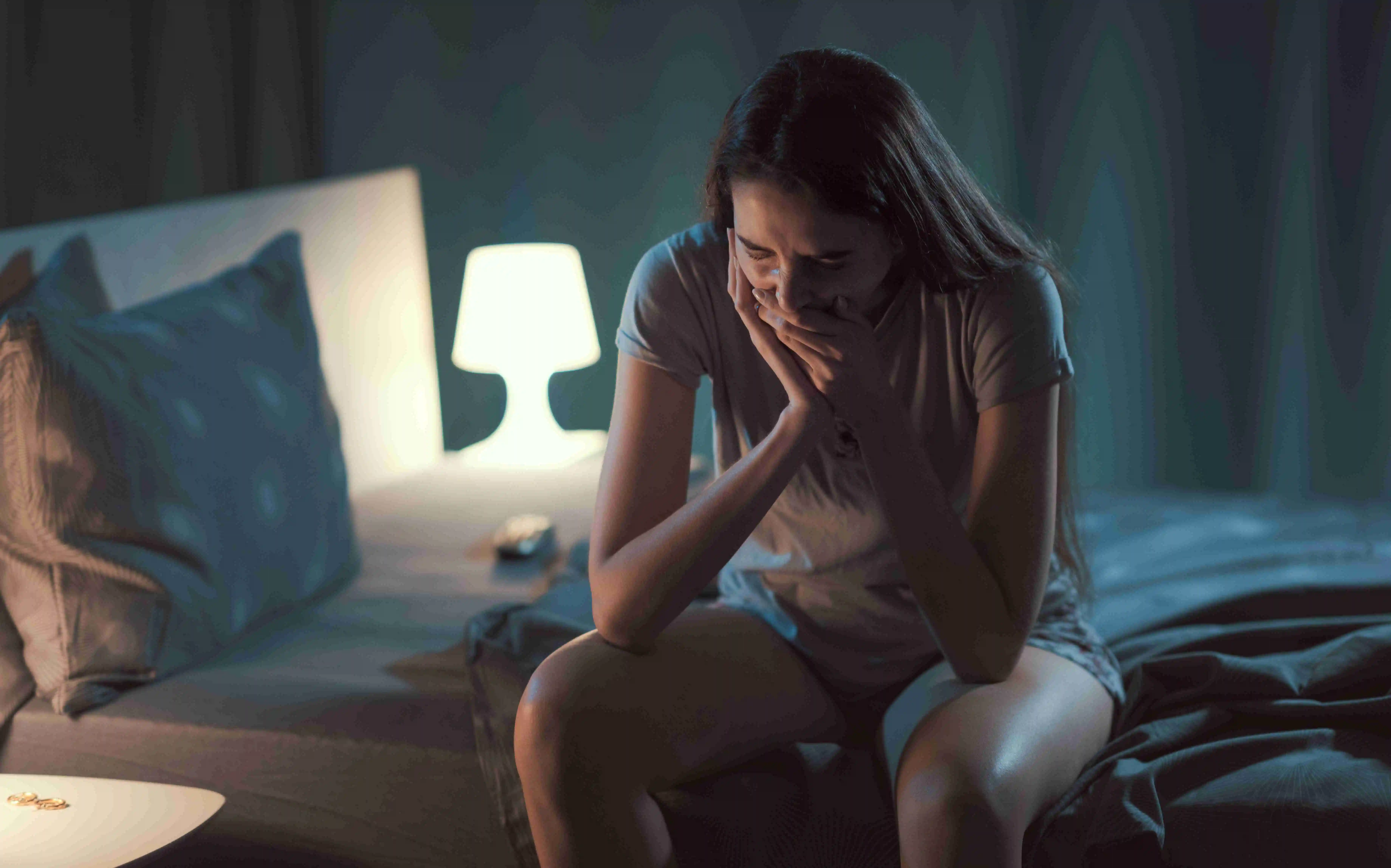 Person sitting on bed in distress, covering their face, suggesting a panic attack or intense anxiety.