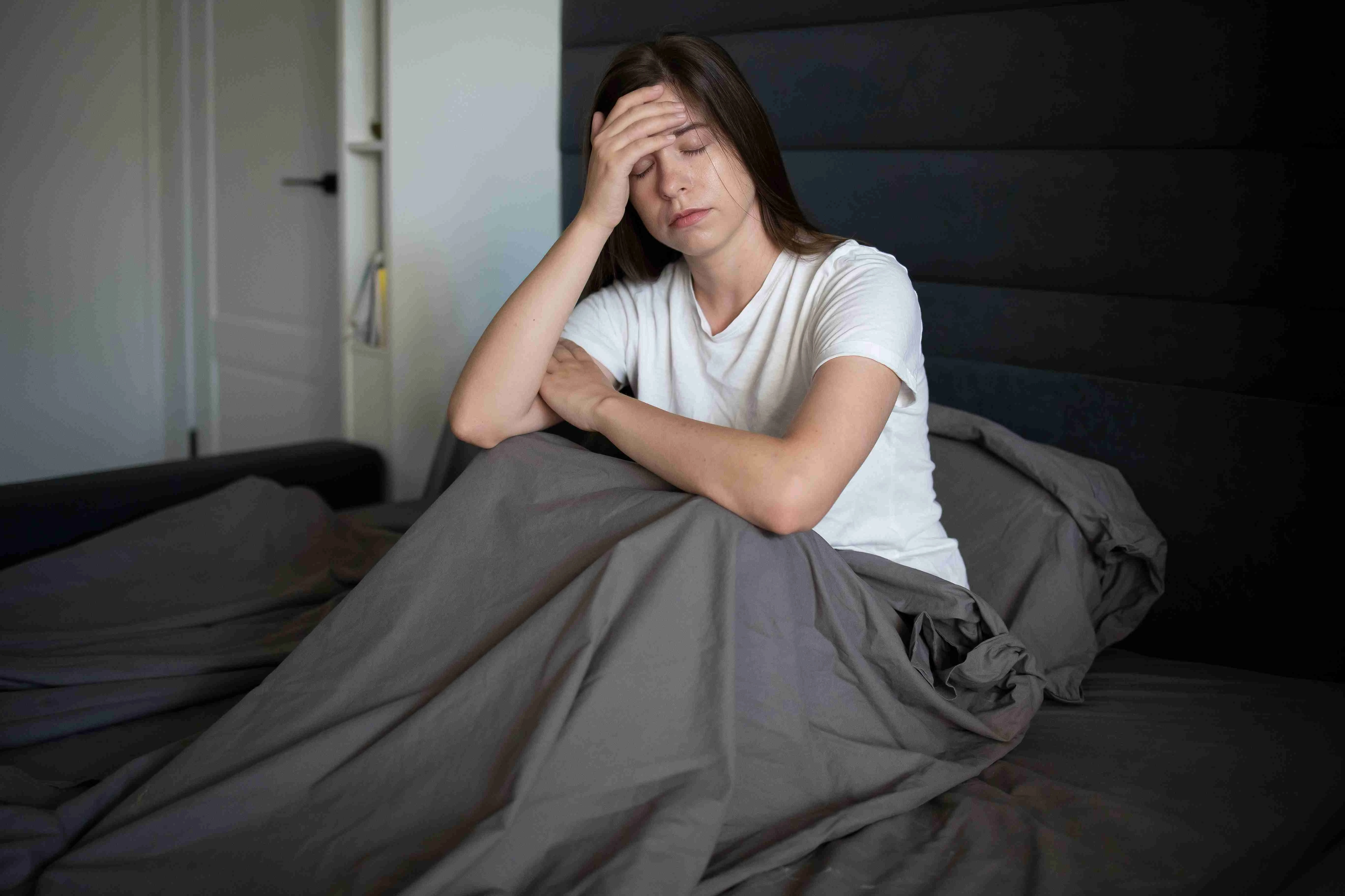 women lying in bed holding her head having a strong headache