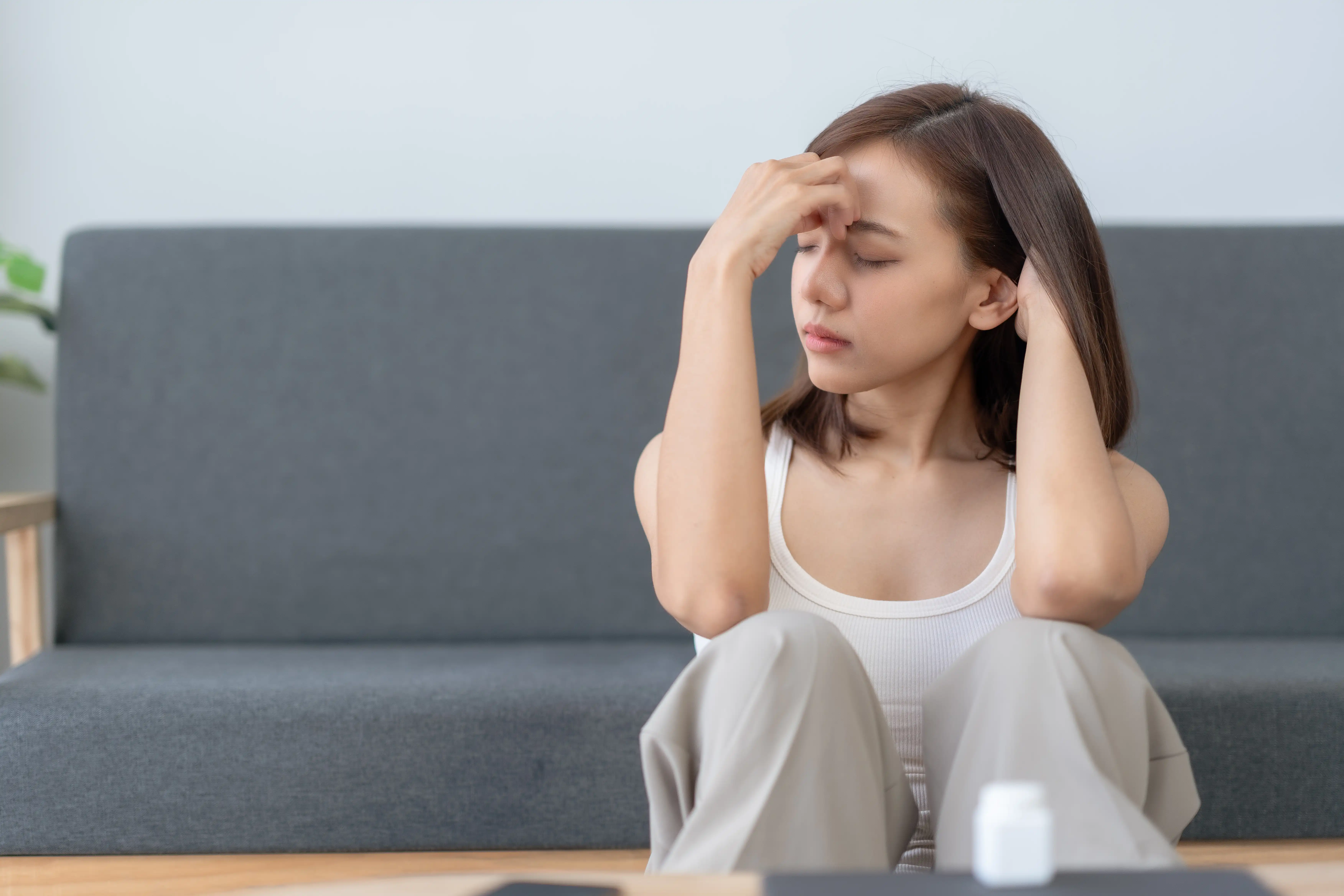 Young woman sitting on the floor, holding her head, appearing stressed or worried, in a home