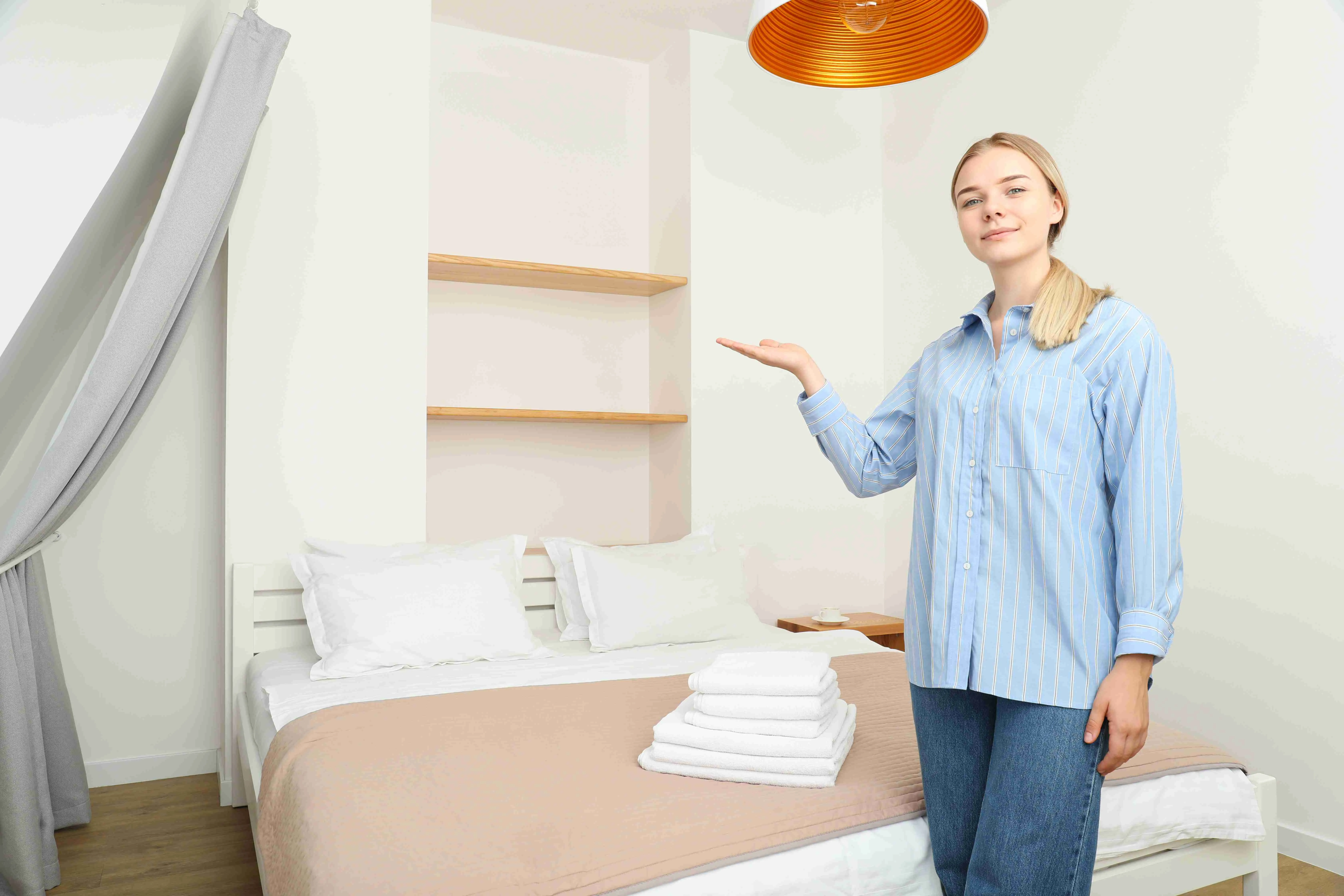 A woman is standing next to a bed in an apartment