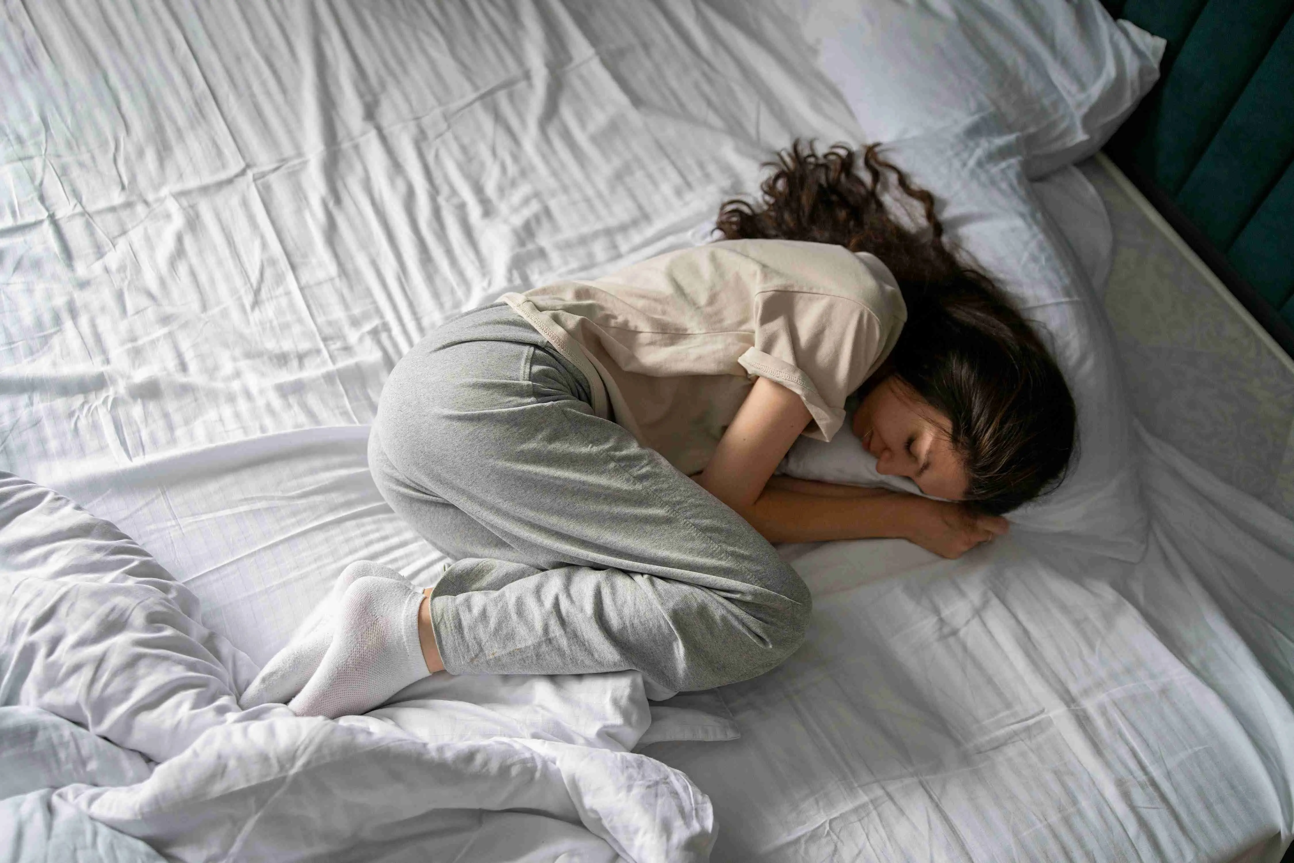 Woman Sleeping in a bad wrong Position on a White Bed in a Dimly Lit Room