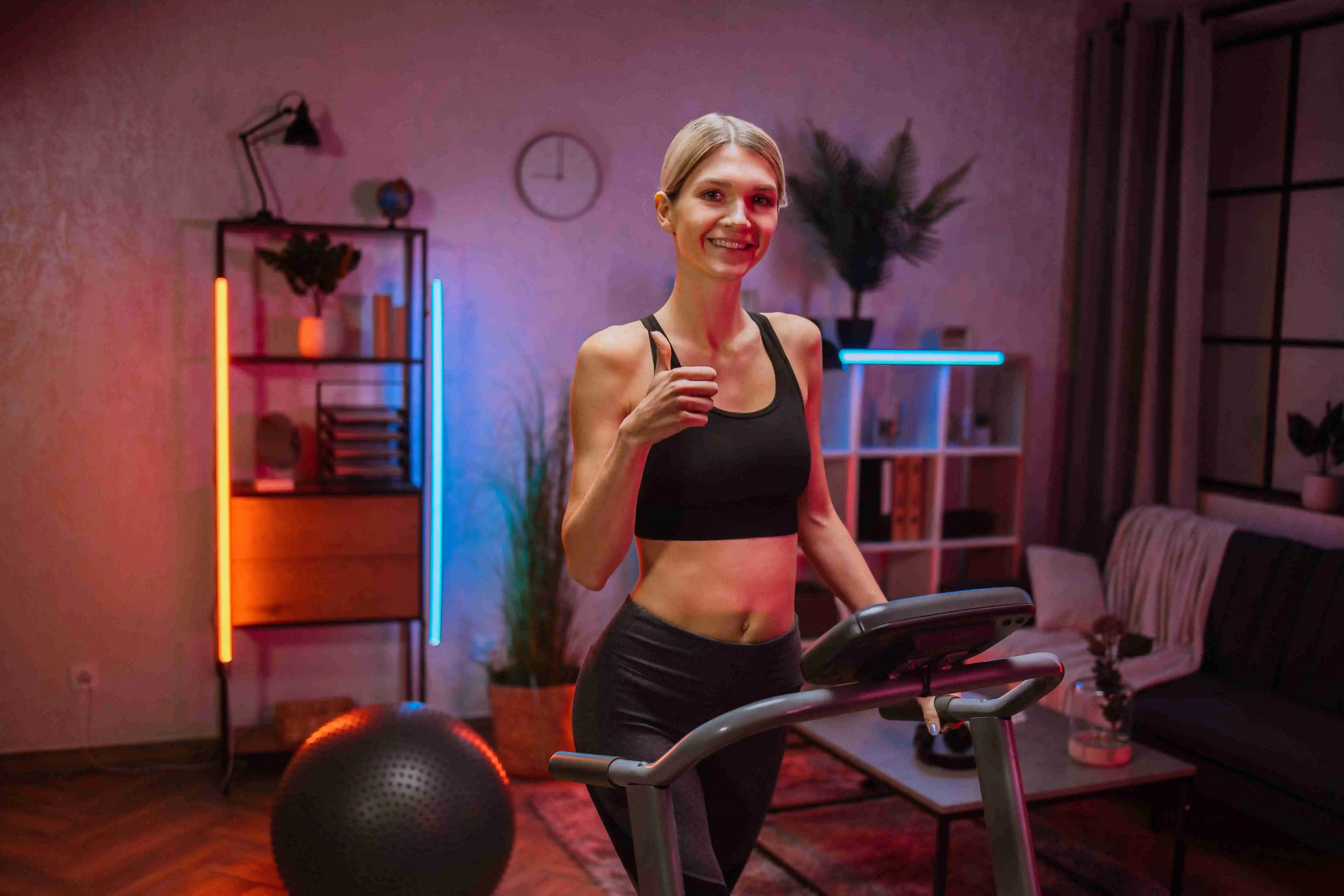 Side view of blond beautiful woman in sports clothes doing cardio training on treadmill at night