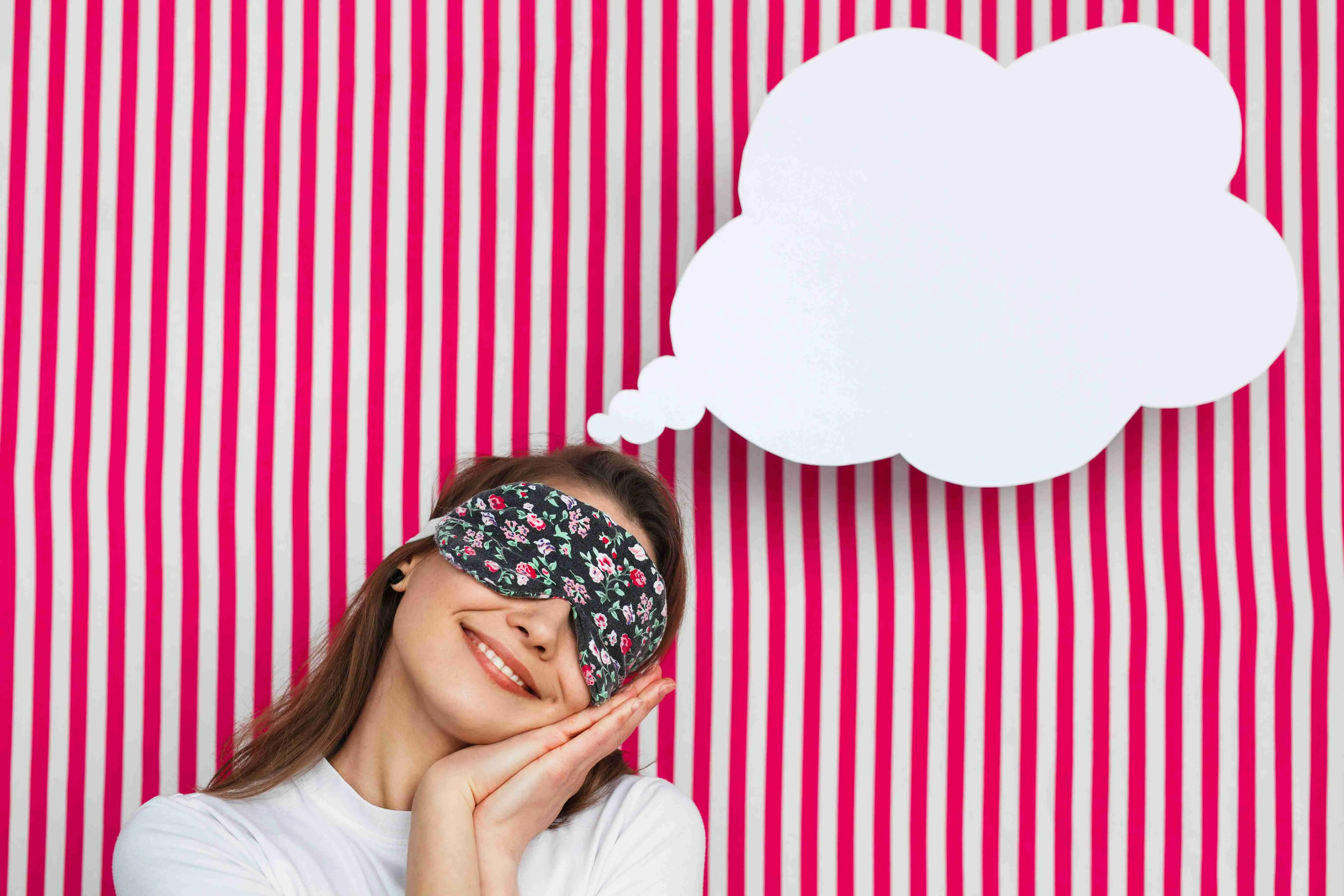 Young lovely girl in sleeping mask posing as sleepy with white speech bubble on striped background.