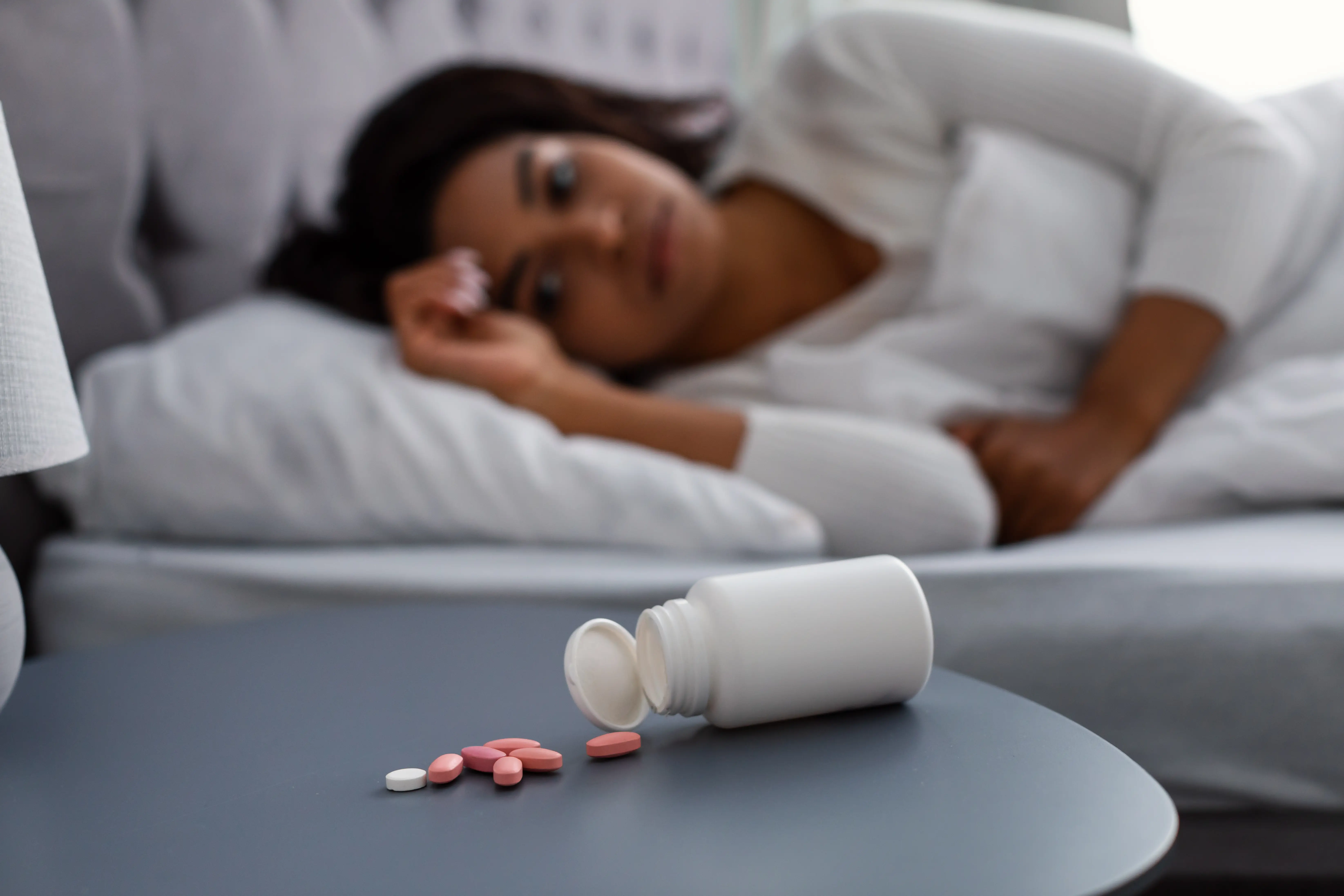 Black woman suffering from insomnia, pills on table