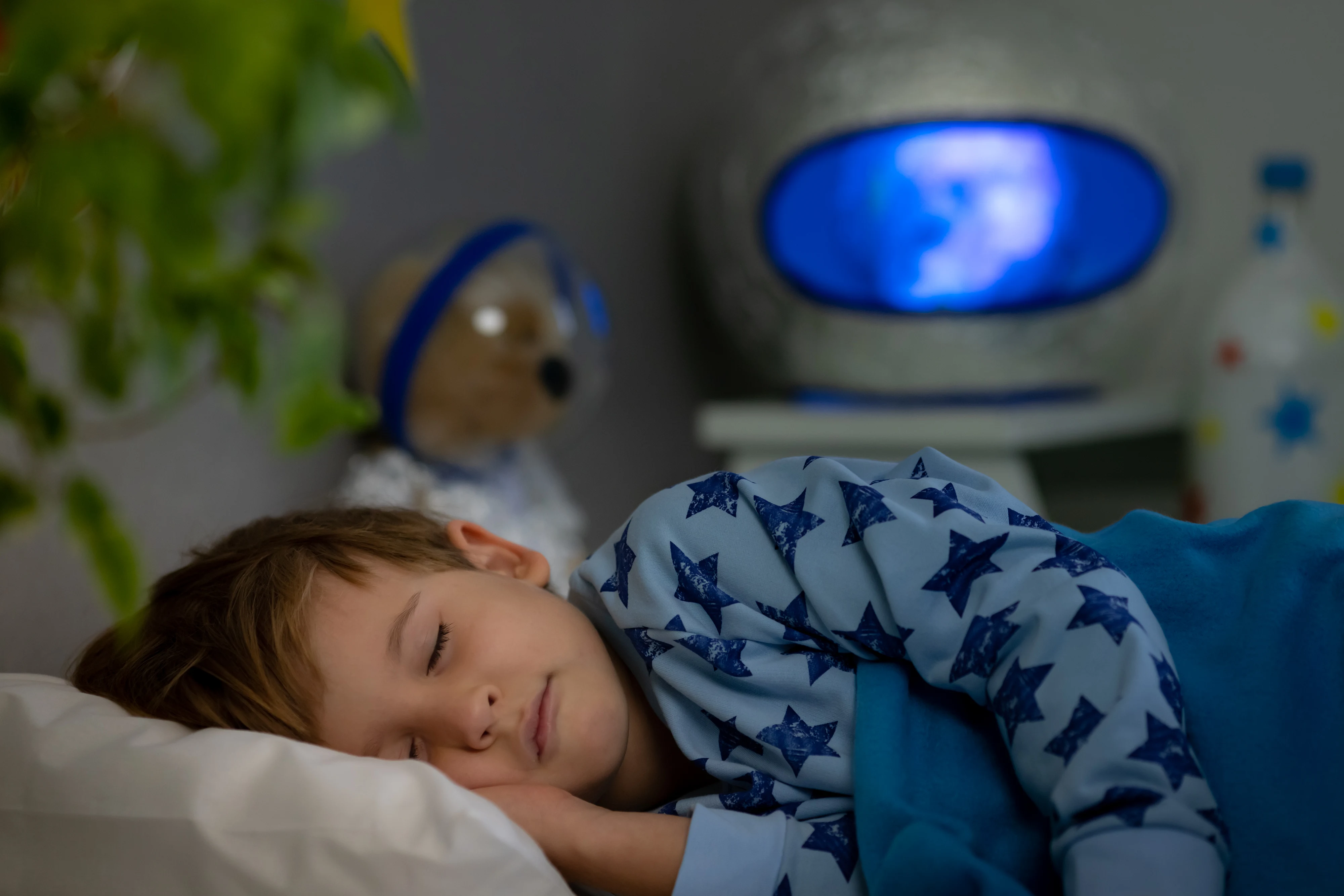 Happy child sleeping with toy rocket and teddy bear. Kid pretend to be astronaut. Imagination and children dream concept