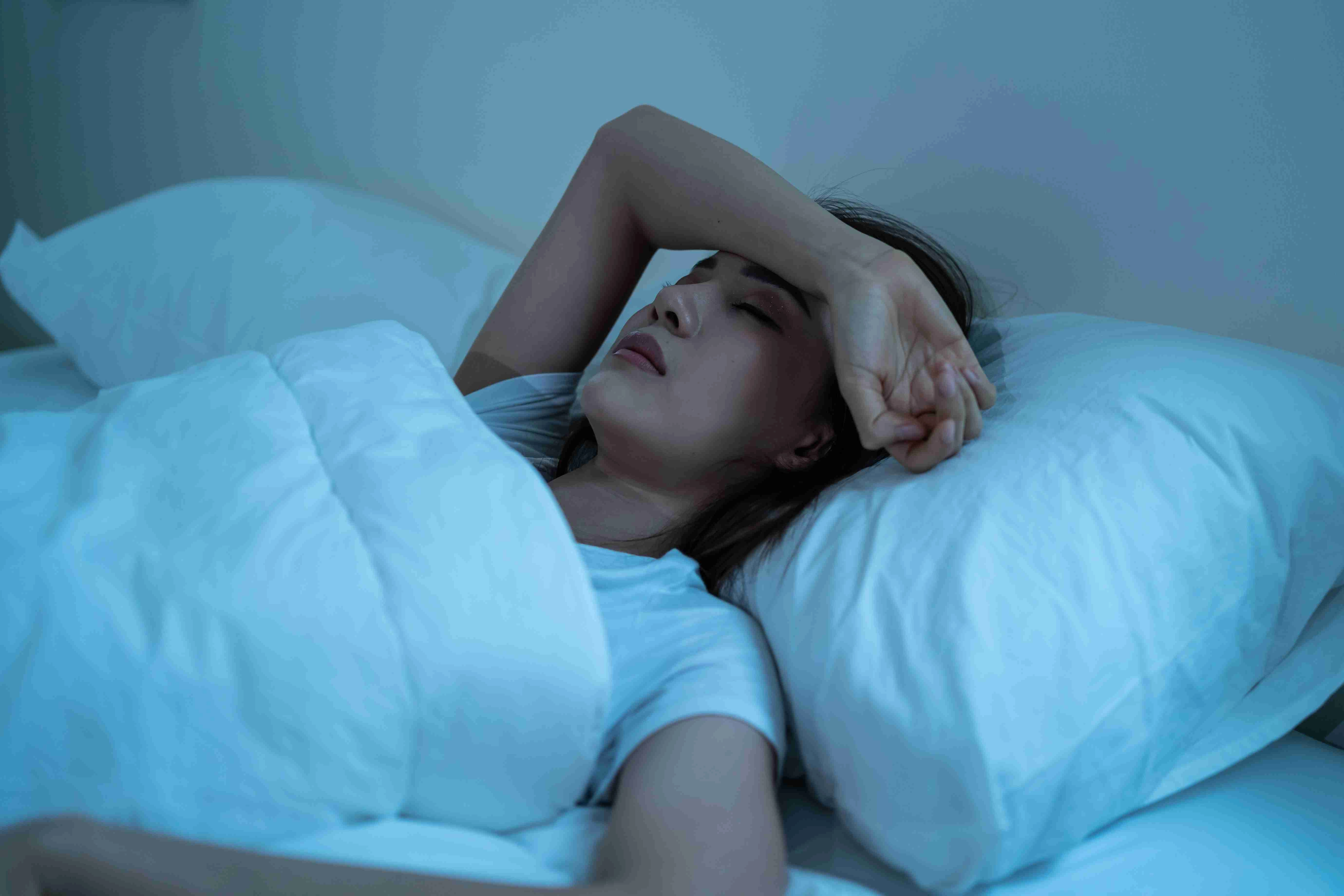 Asian frustrated girl in pajamas lying awake on bed in dark night time