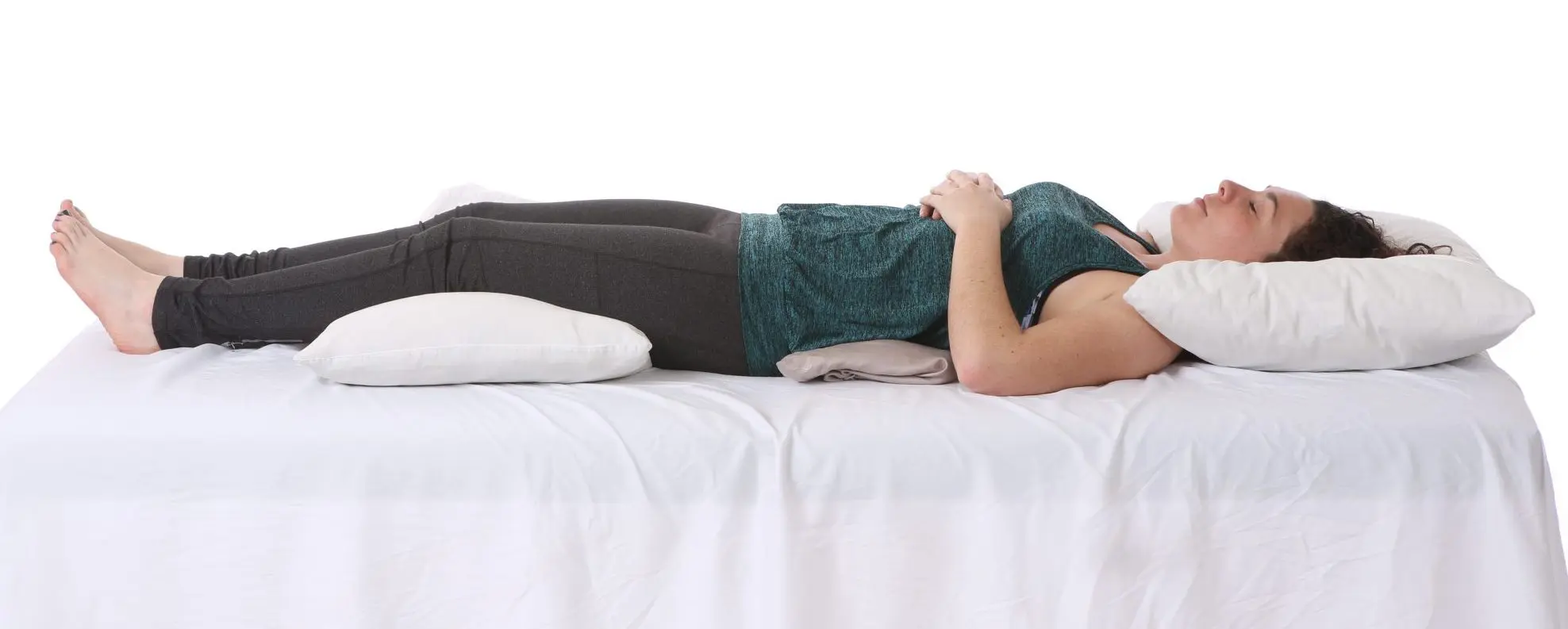 A person lying on their back on a white bed, hands clasped on their stomach, with a pillow under their head.