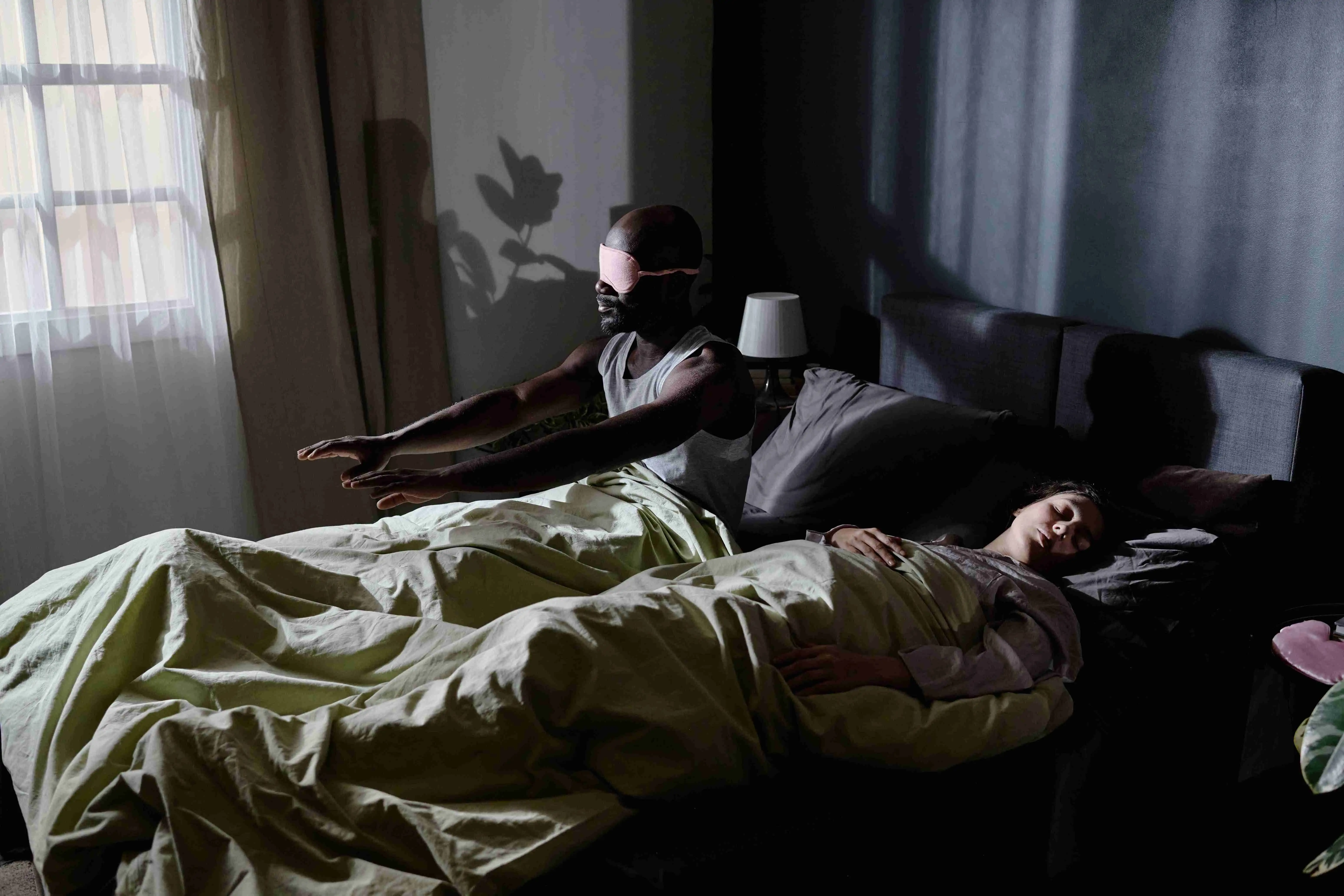 High angle shot of African American man suffering from sleepwalking getting up from bed while wife sleeping