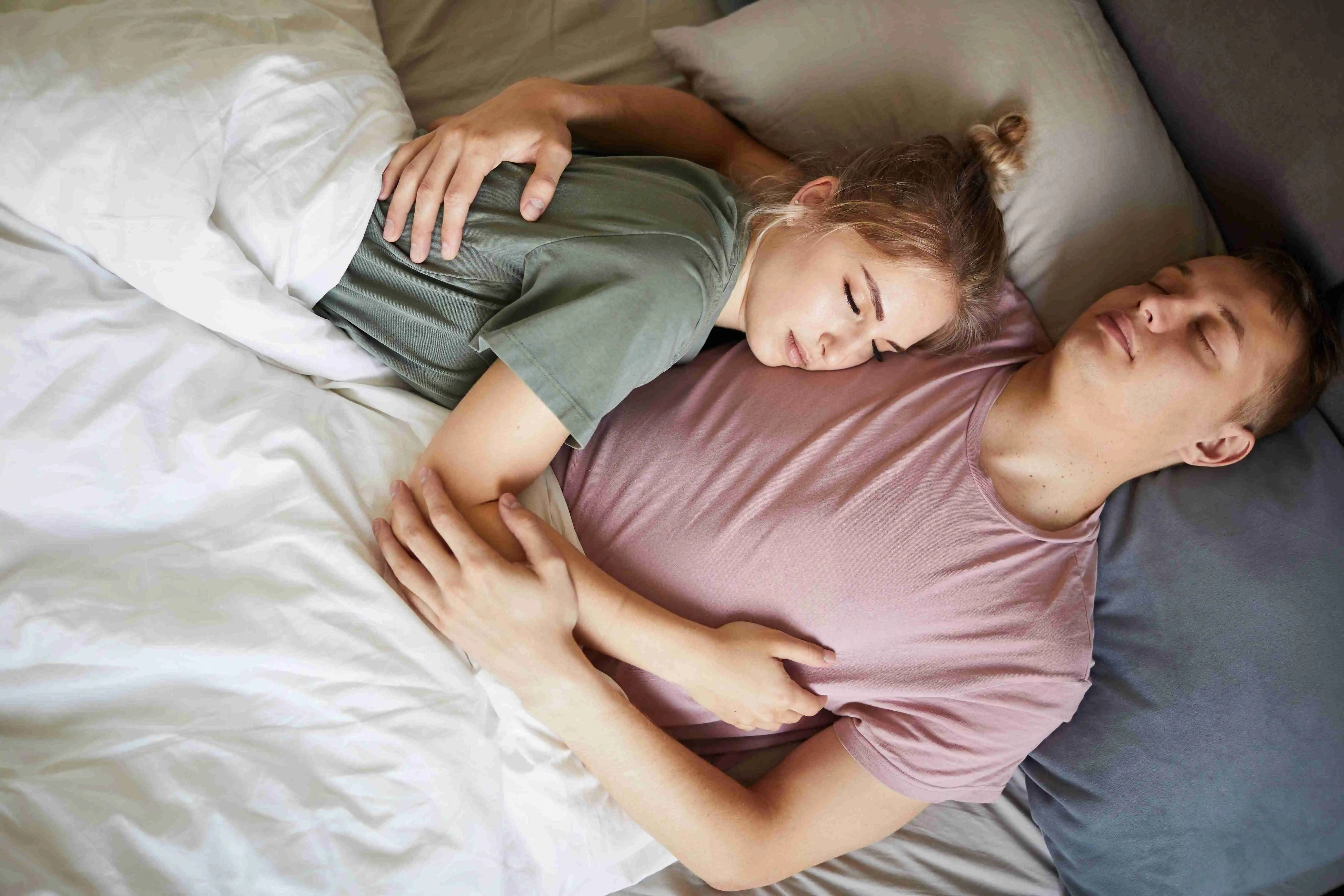 Peaceful young spouses in t-shirts sleeping close to one another under blanket at night