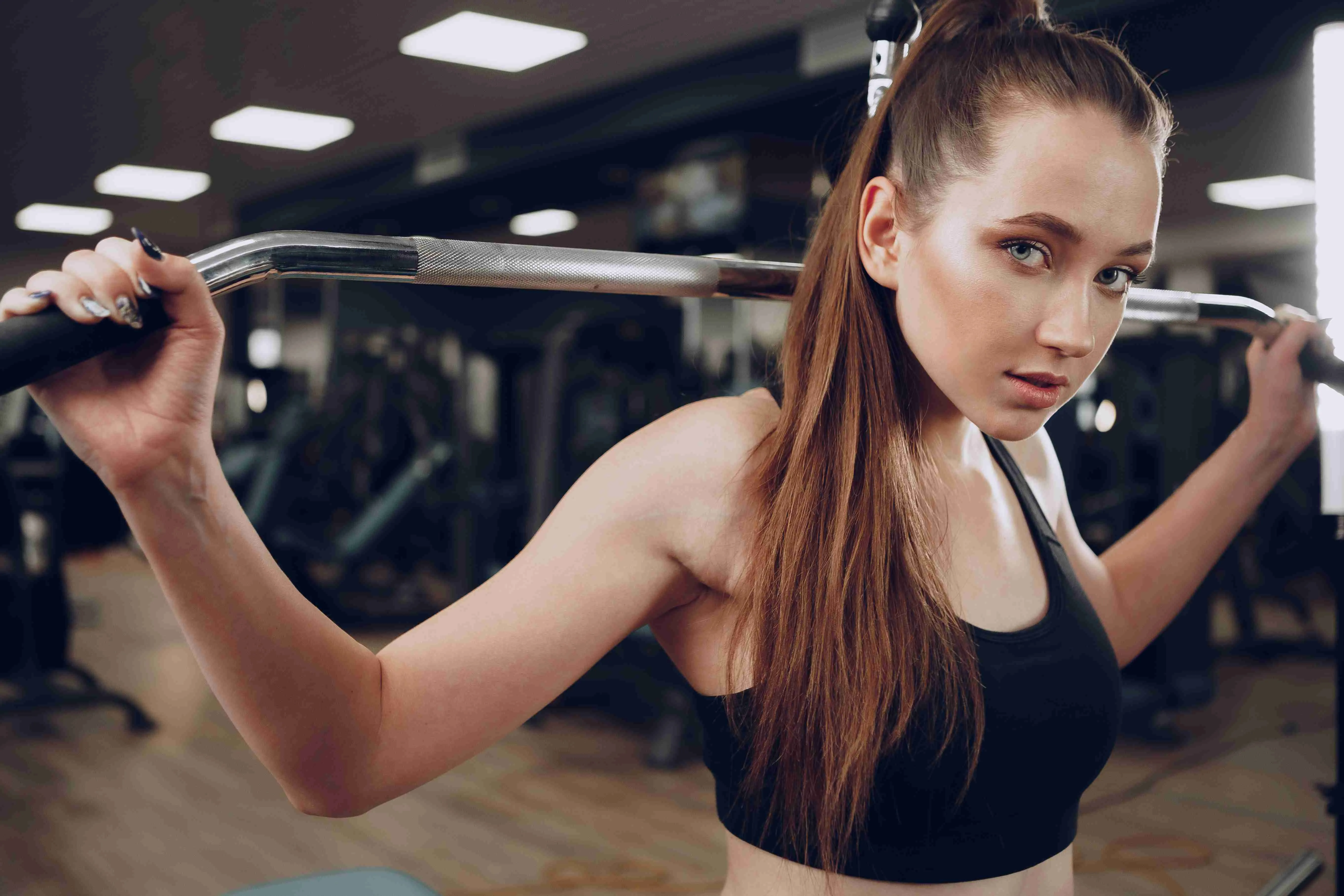 Attractive young woman doing exercises for the muscles of the arms and back in a gym close up