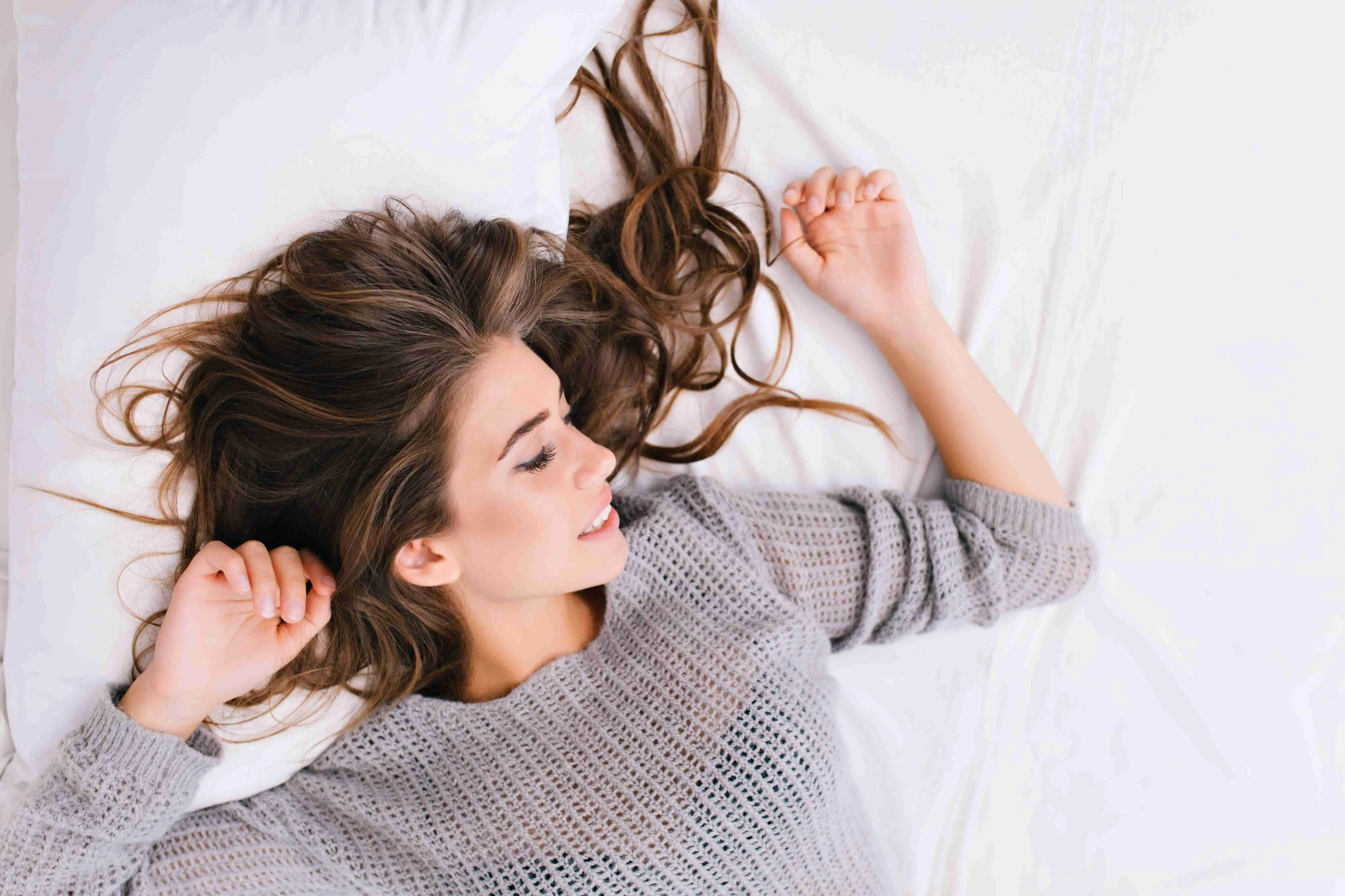 Up portrait cheerful girl with long brunette hair relaxing on white bed