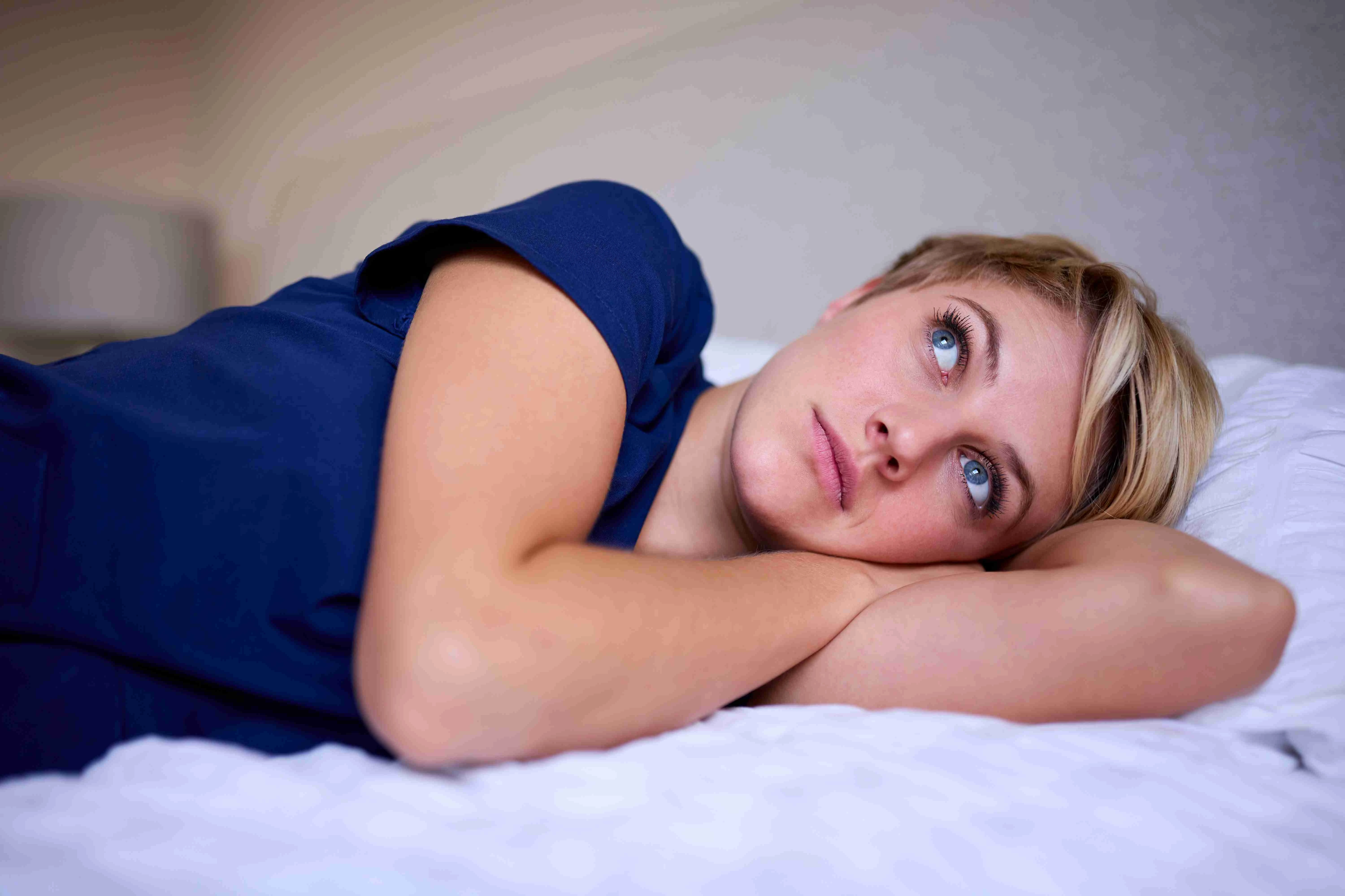 Thoughtful Woman Wearing Medical Scrubs Lying On Bed At Home