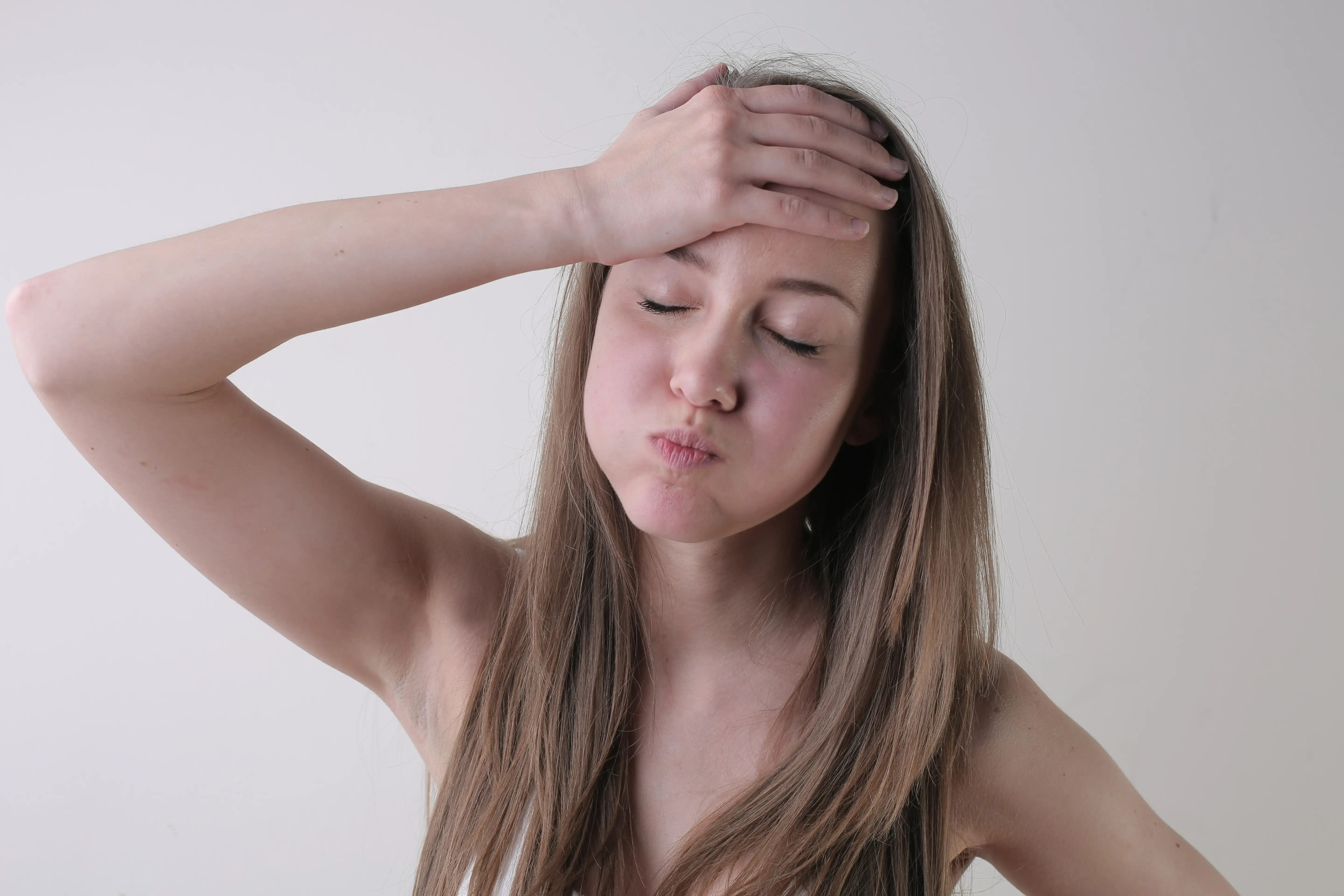 A portrait of an attractive young female with an annoyed face standing against a white wall