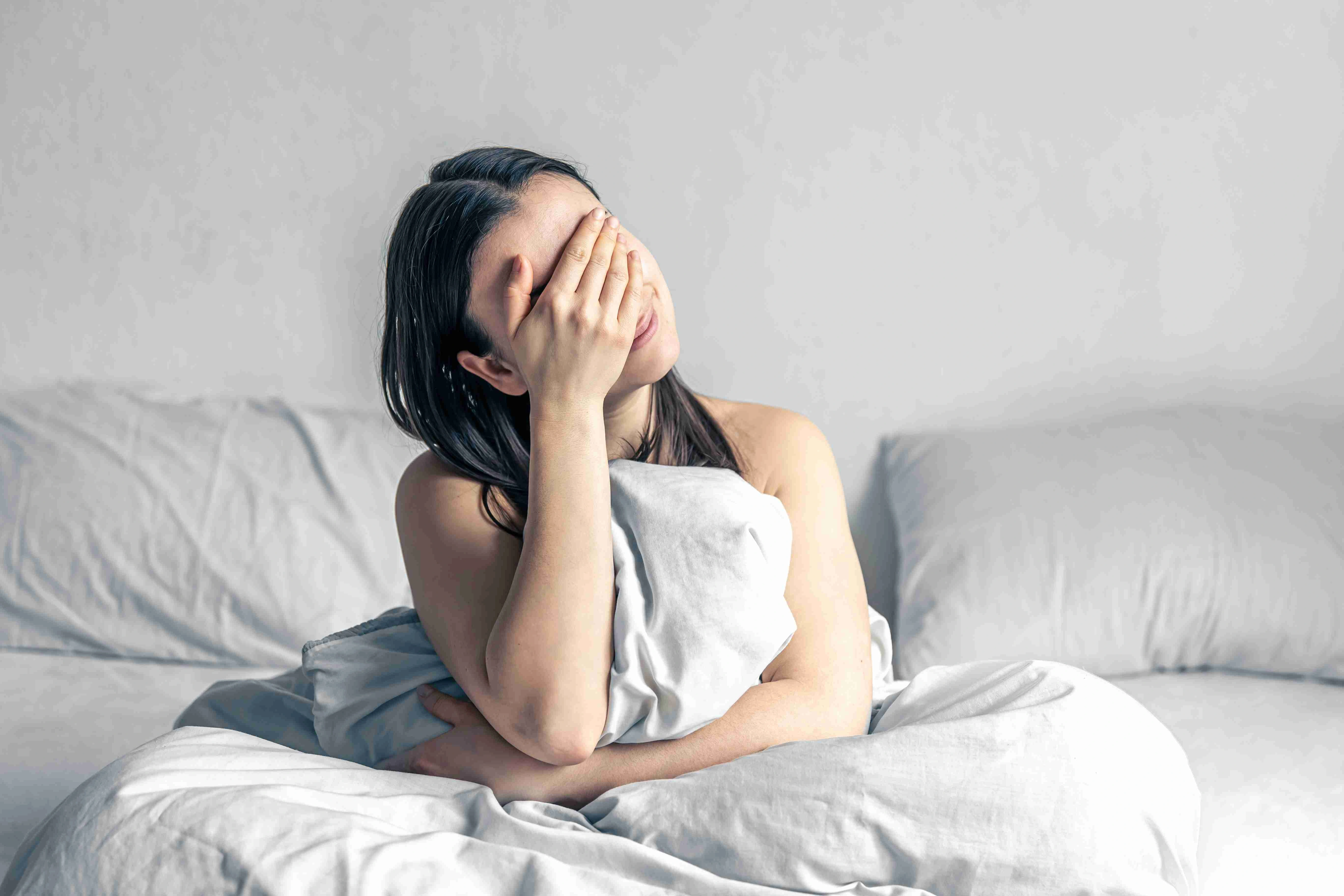 Beautiful young brunette woman sitting in bed in the morning, awakening from sleep.