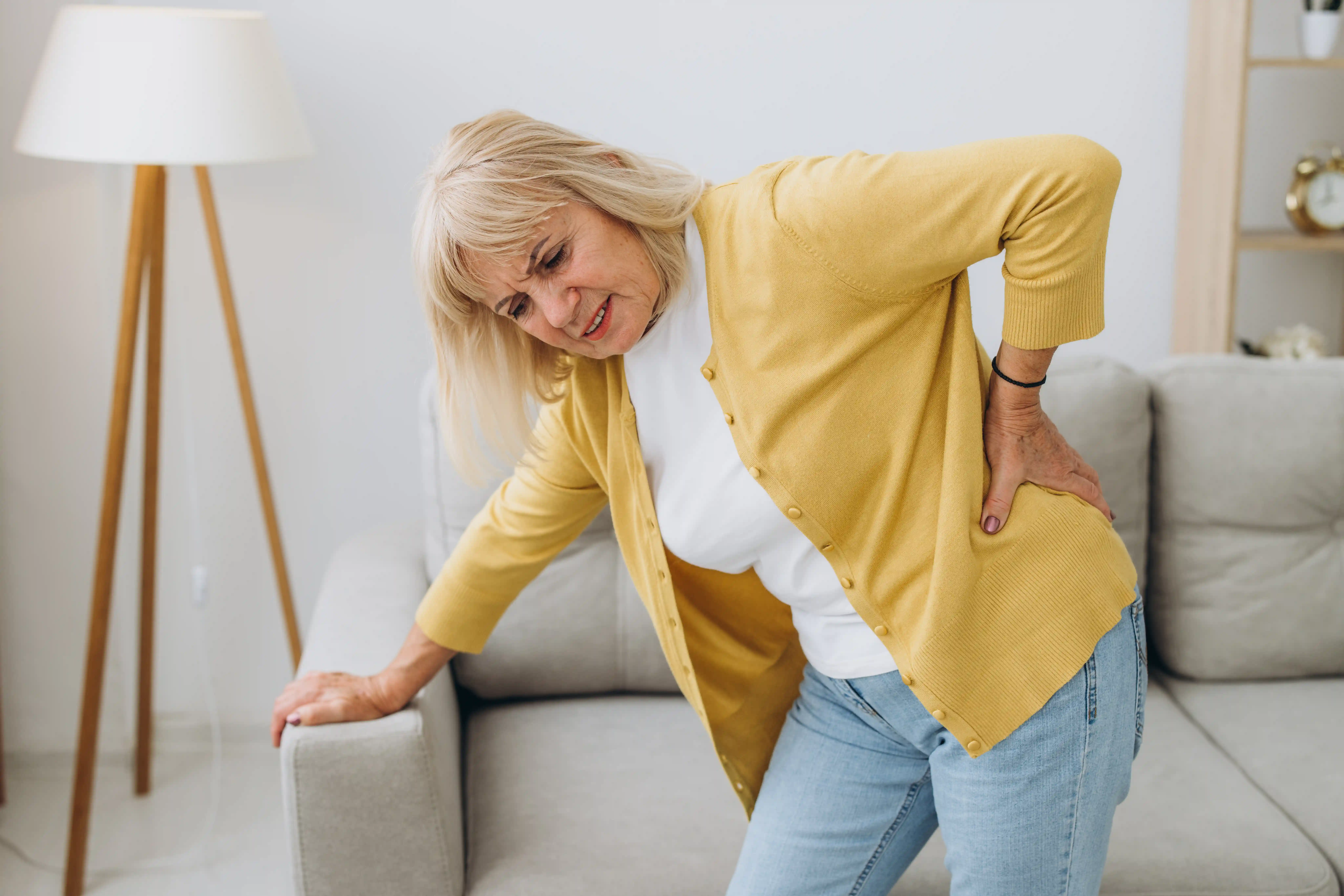 Senior woman having backache and touching her back in living room at home