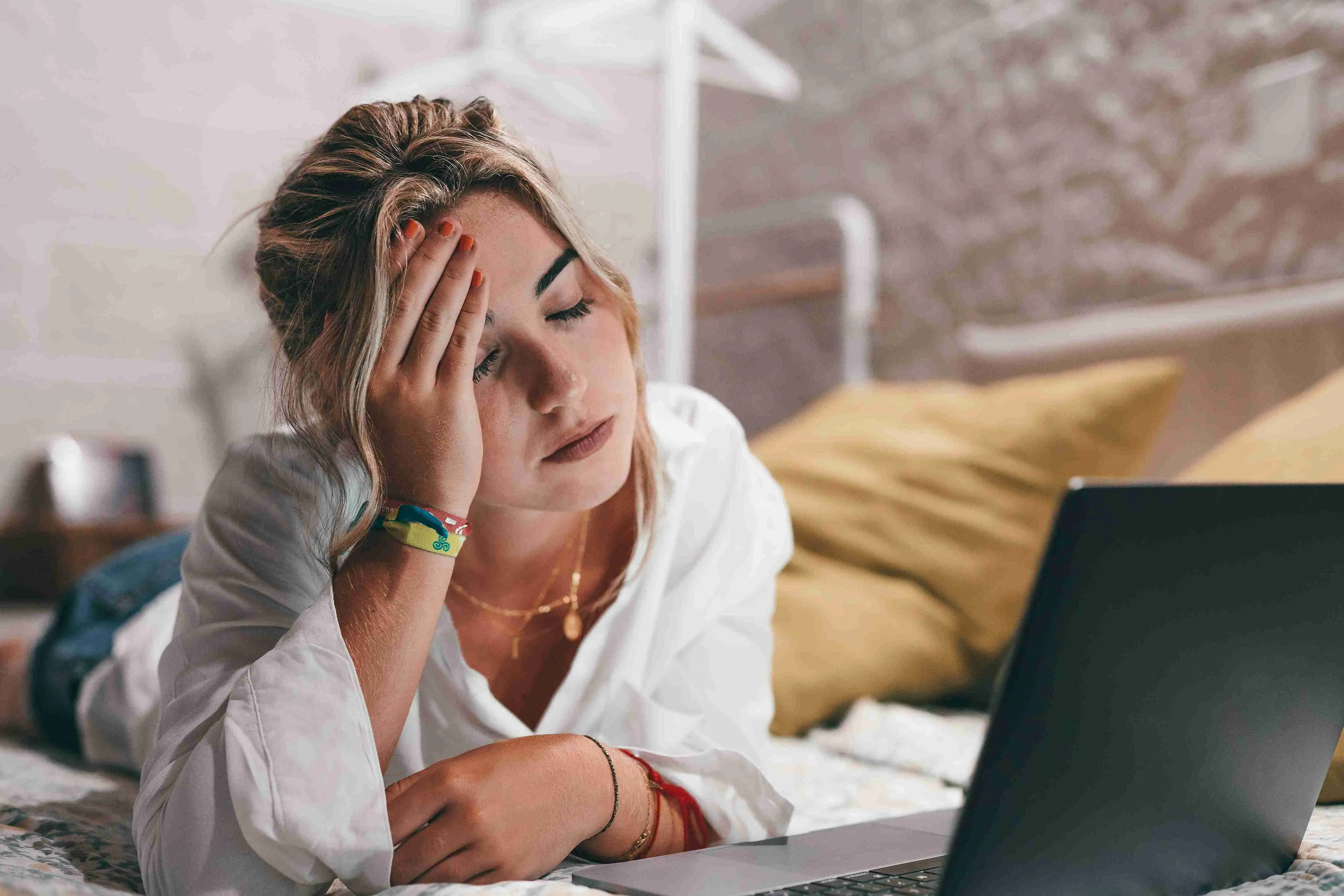 Close up of one young woman using laptop at home in bedroom suffering bad headache