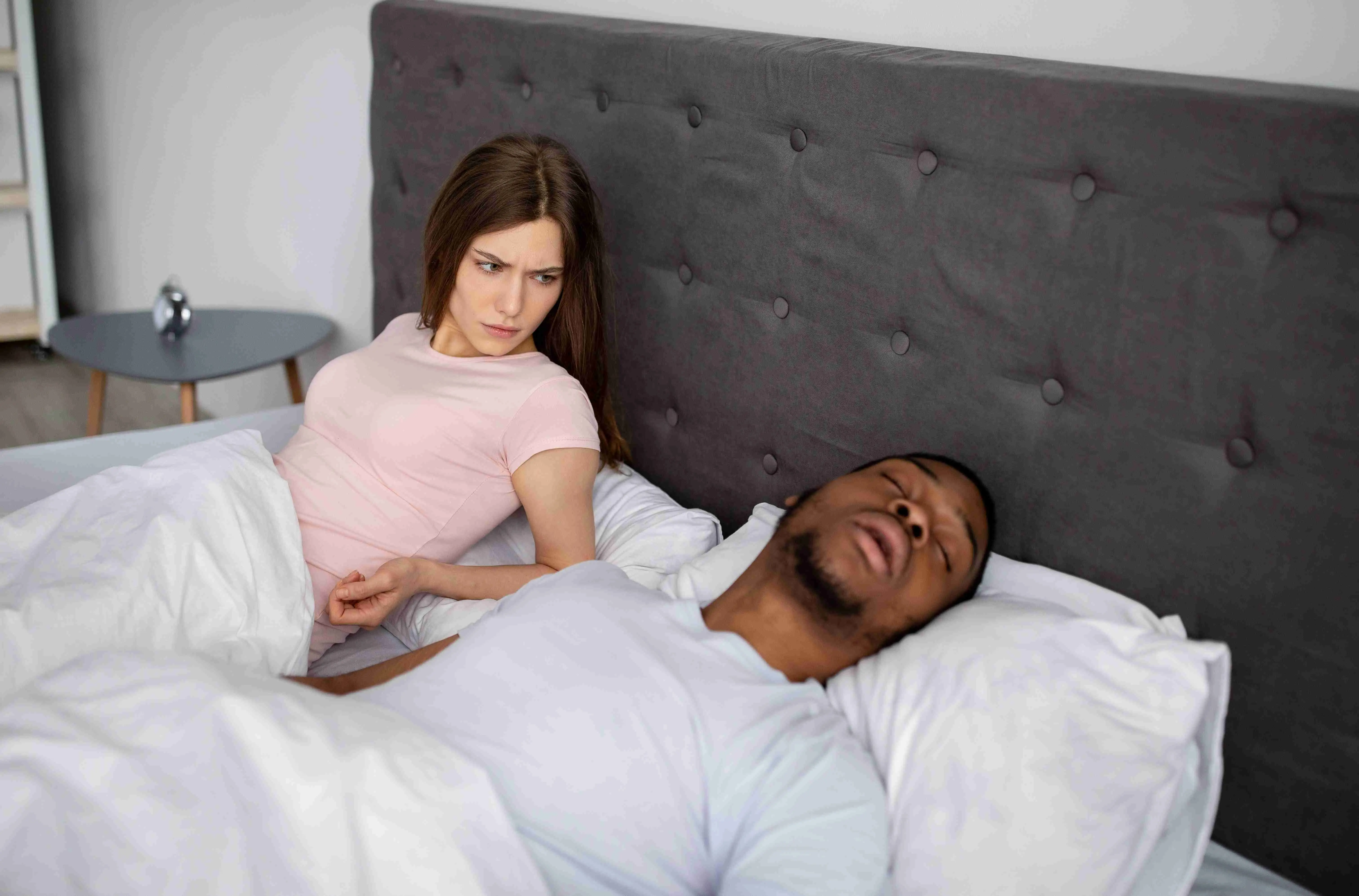 Millennial black man snoring and bothering his irritated sleepless wife in bed at home