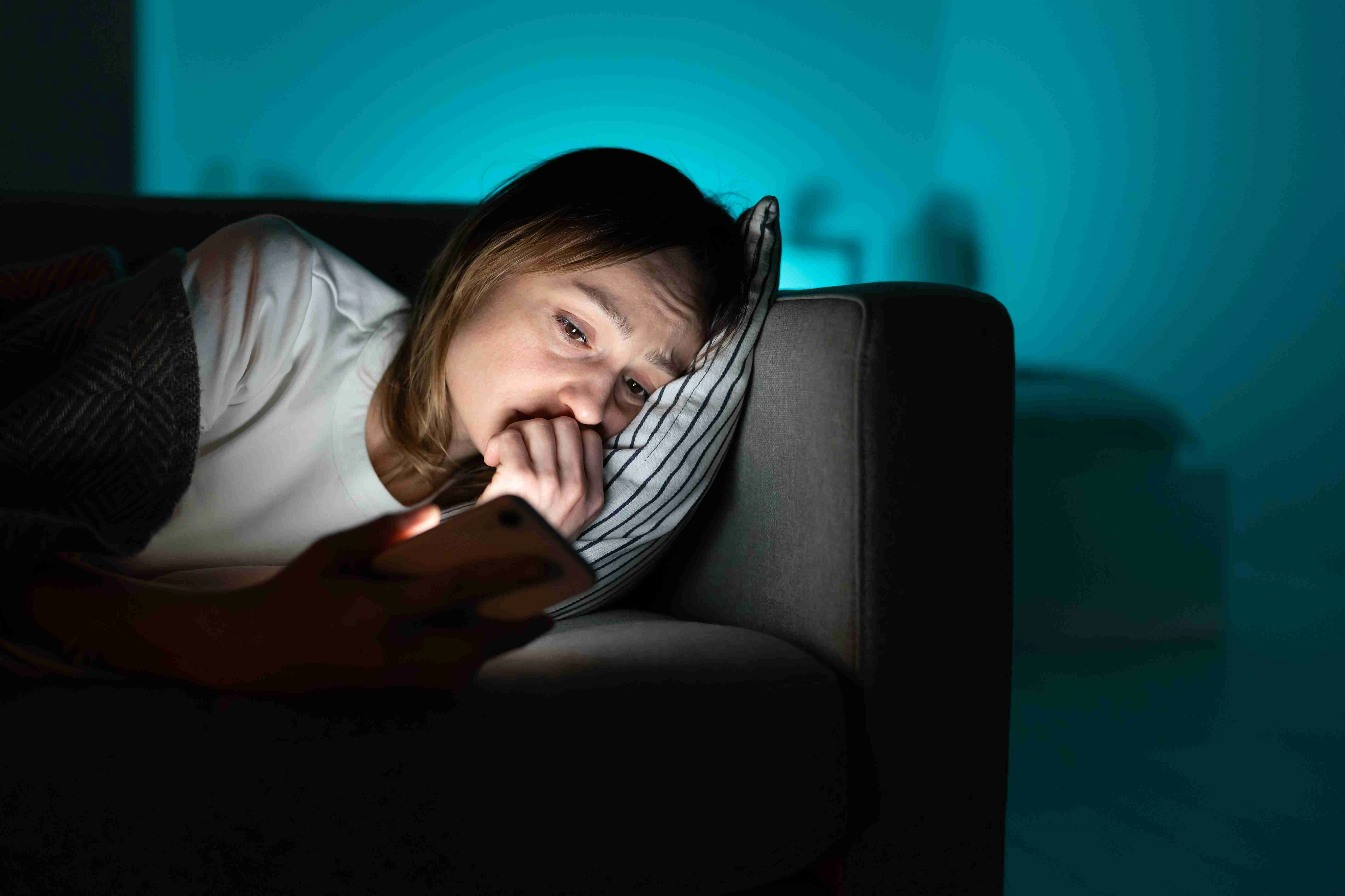 Anxious female with sleep disorder look at smartphone screen in dark room