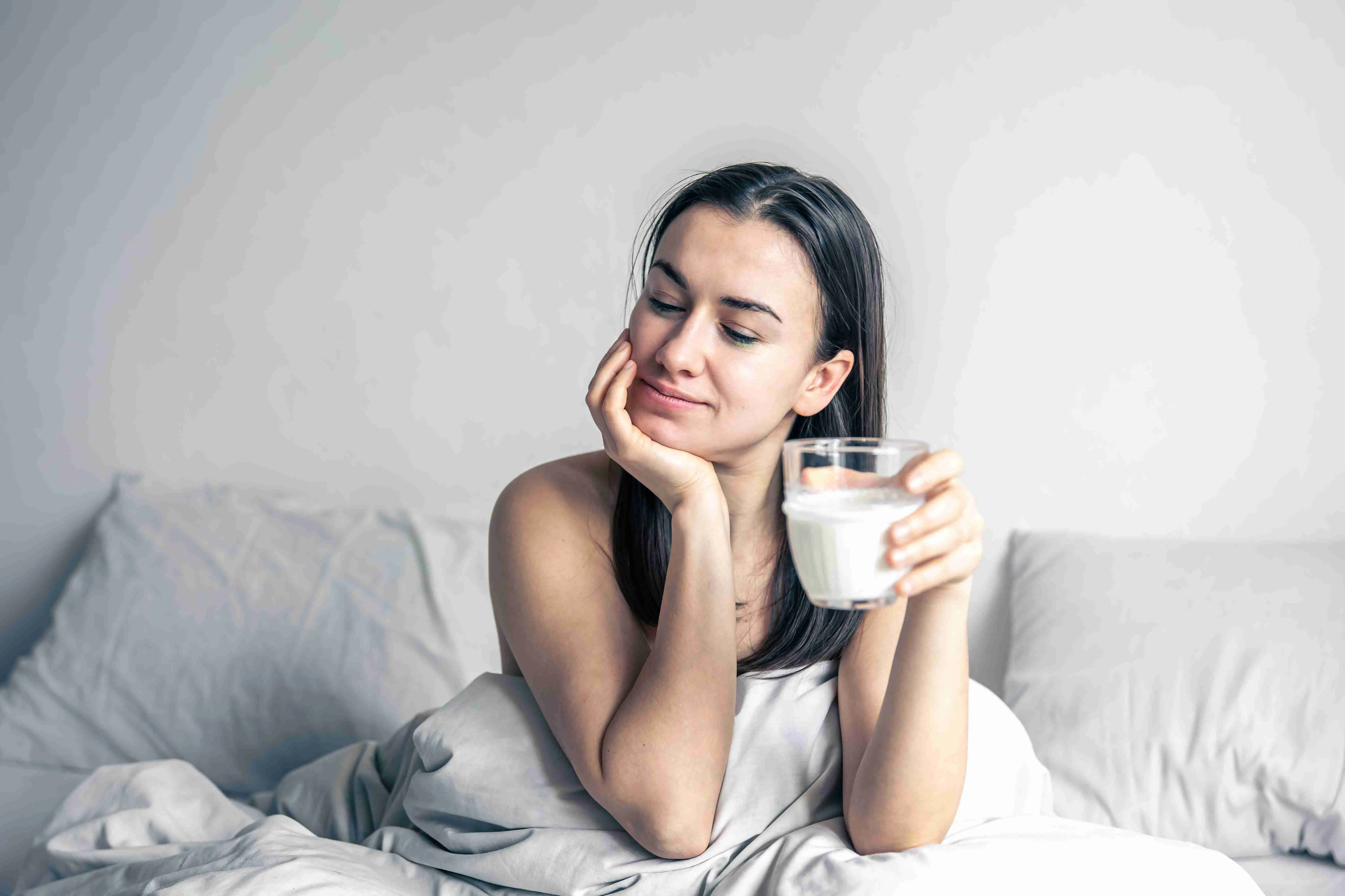 Beautiful young woman in white bed with glass of milk.