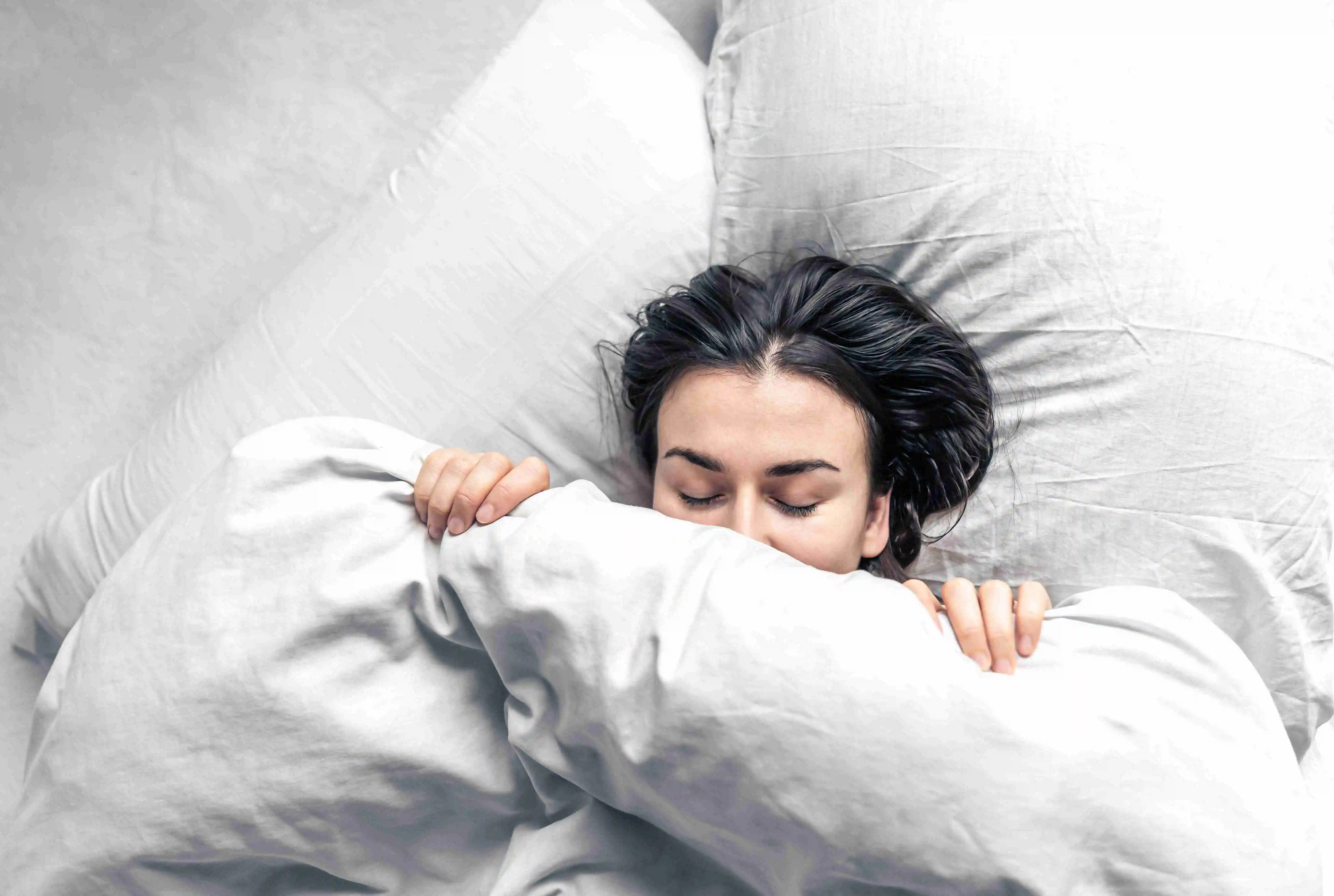 A beautiful young woman sleeps in a white bed.