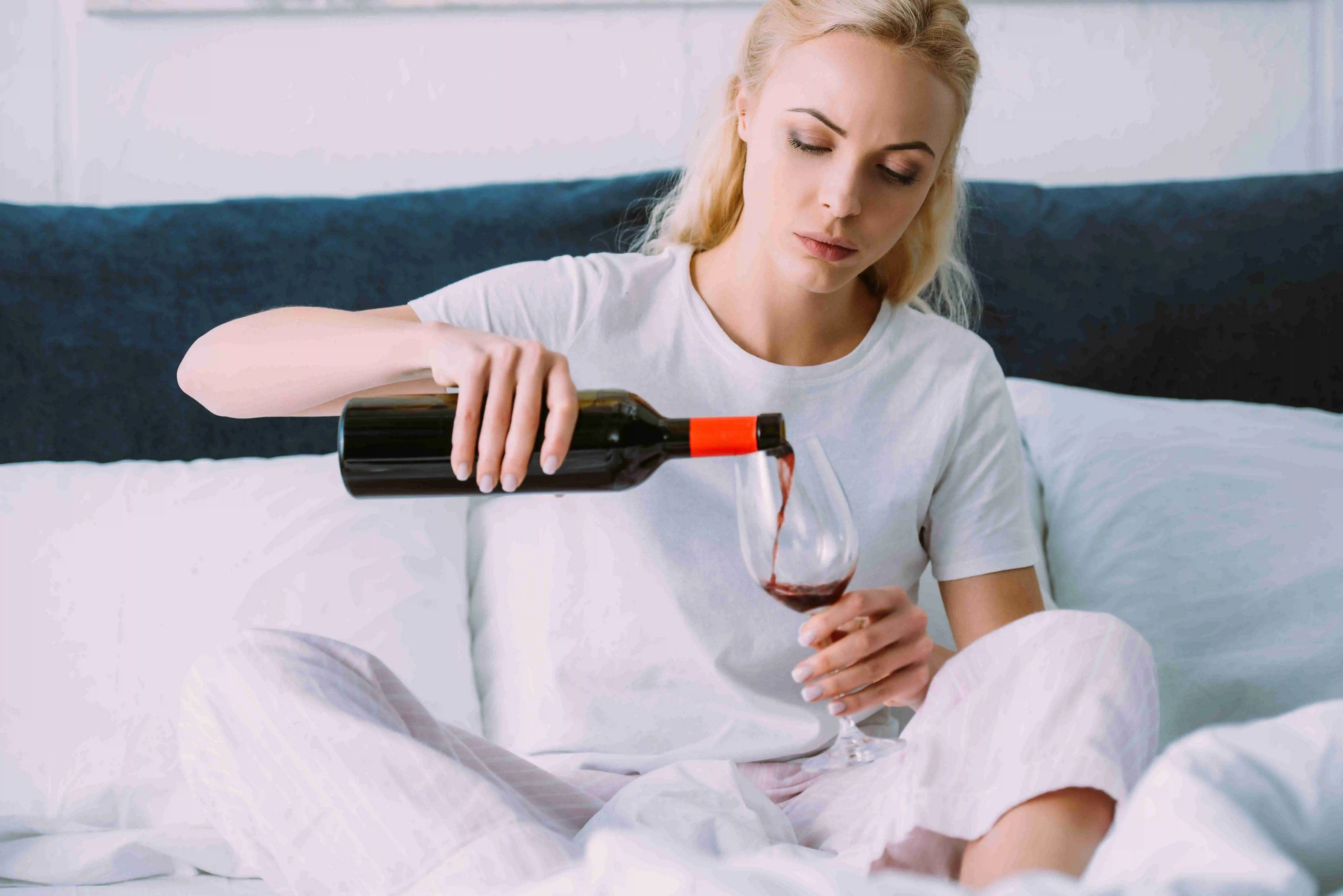 sad woman in pajamas pouring red wine in bed at home