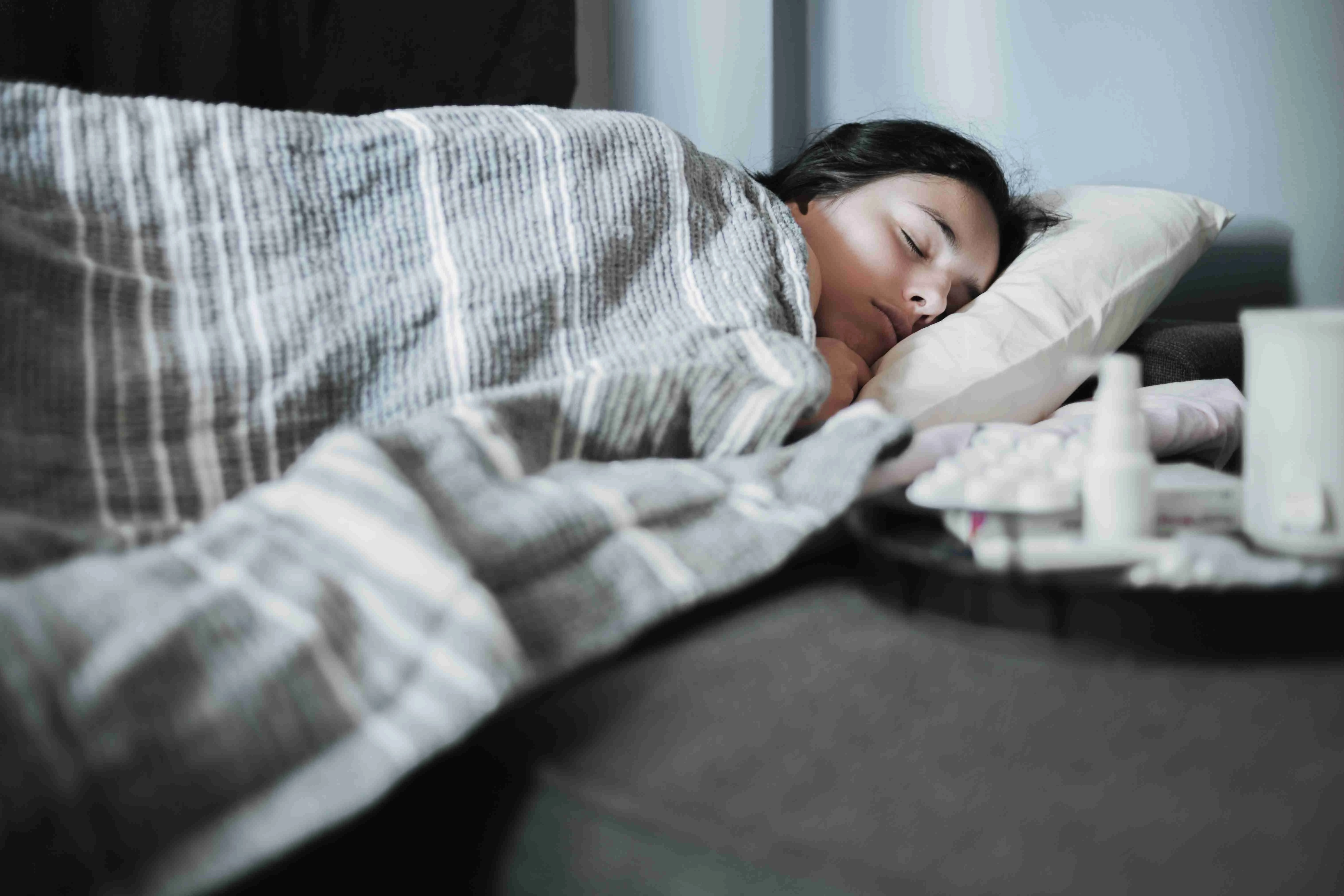 A girl suffering from a seasonal cold lies in bed. Antiviral drugs on a tray