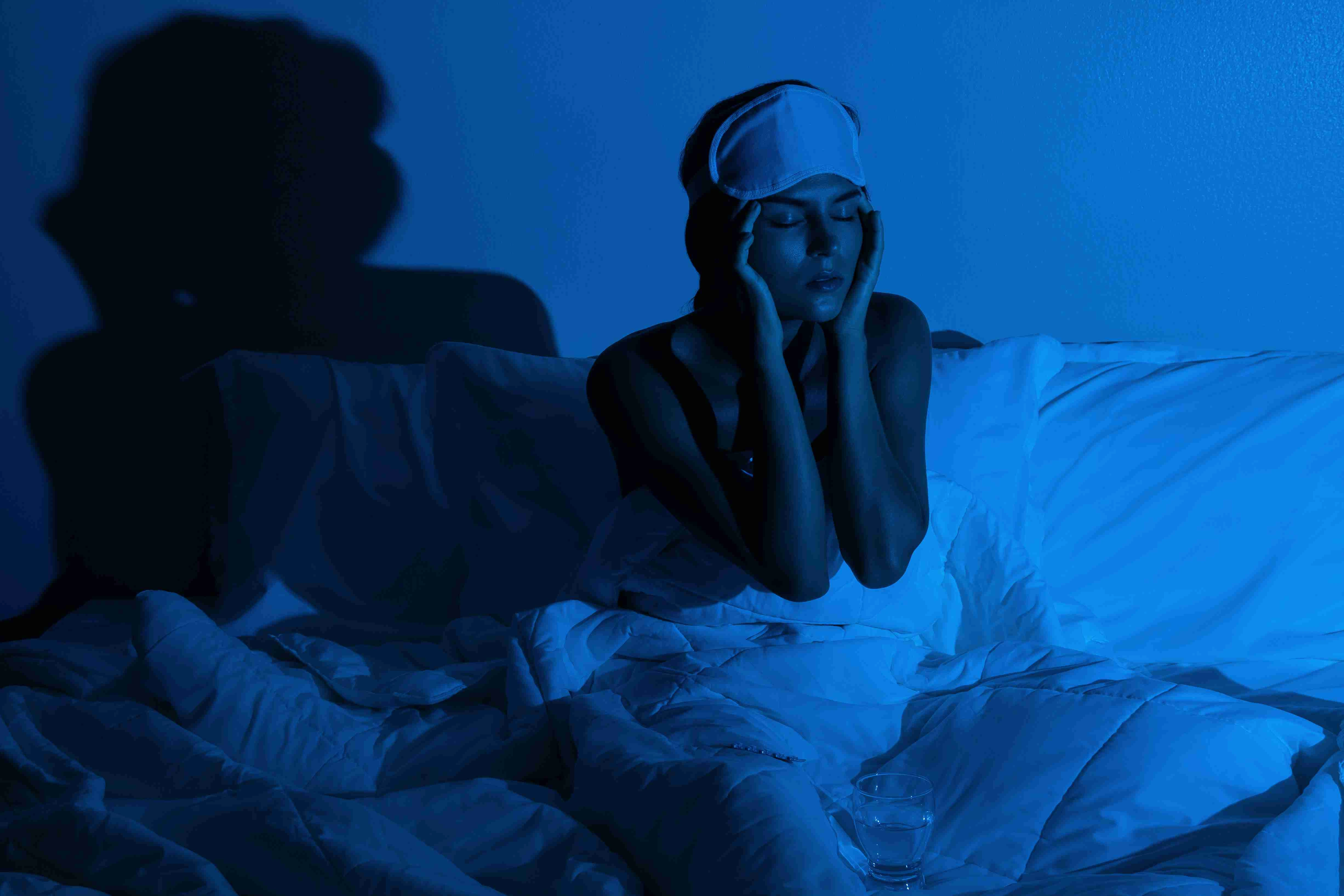 Young woman in the dark bedroom with a glass of water and sleeping pills