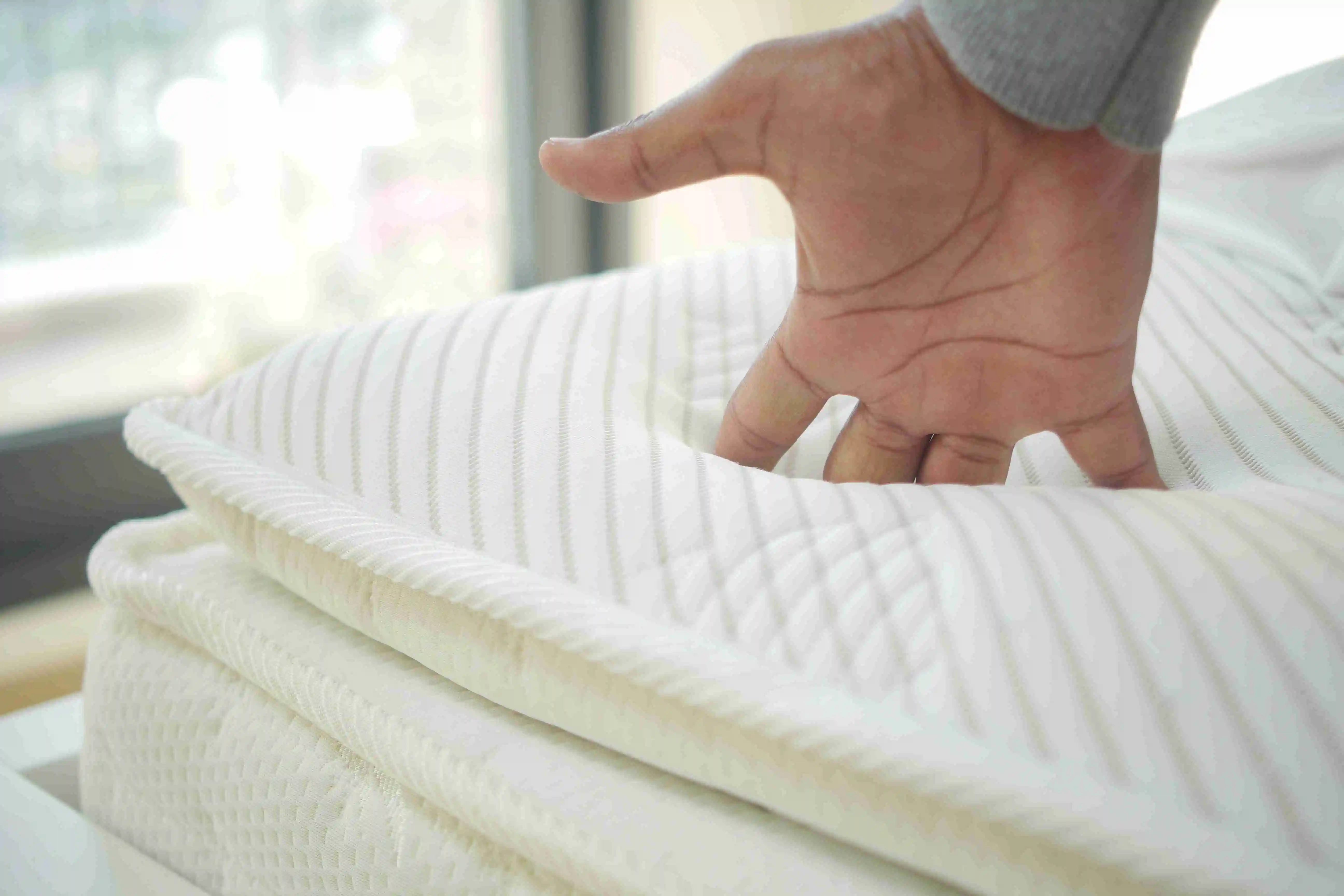 Hand touching and pressing orthopedic mattress on bed.