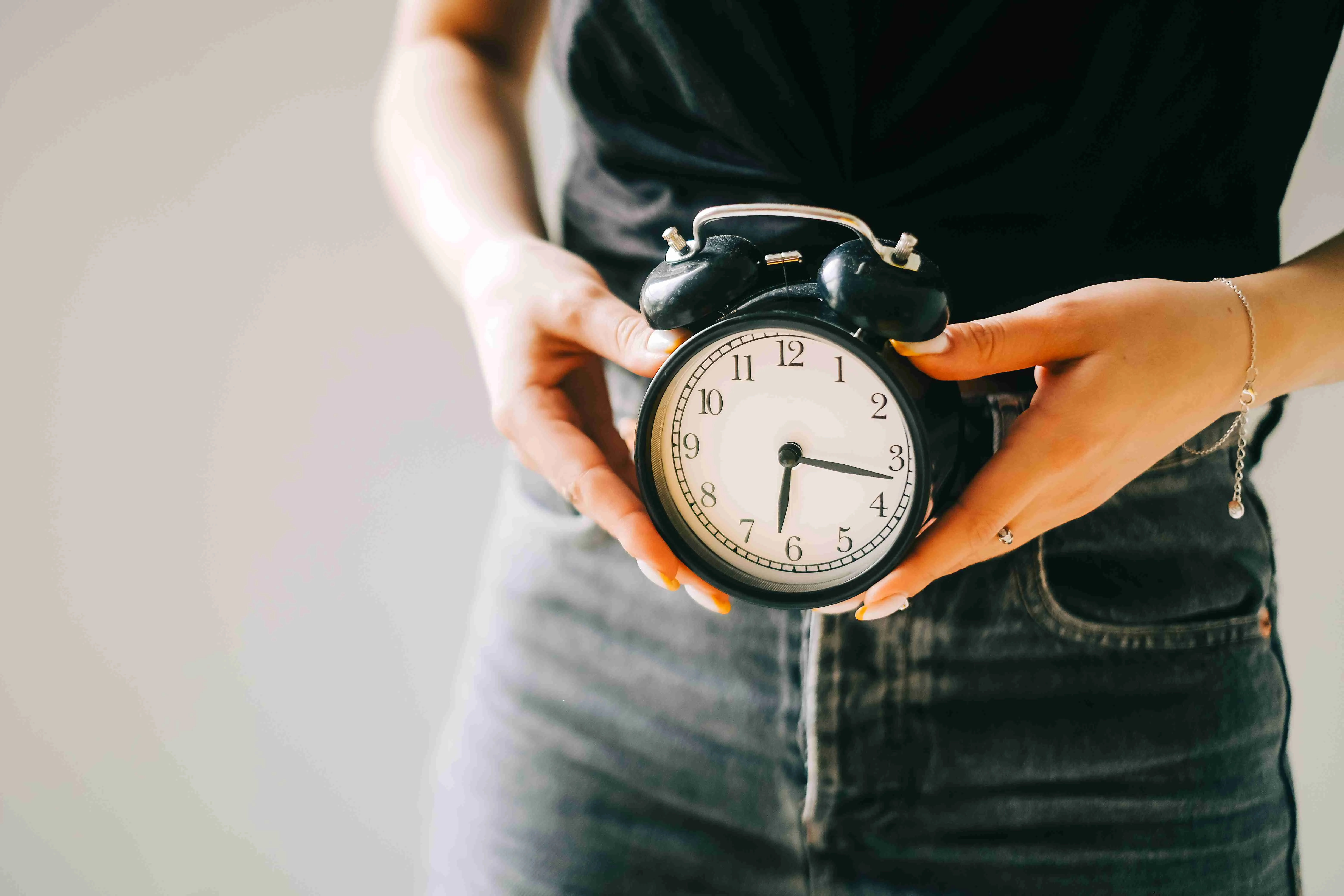 Young Caucasian woman holding black alarm clock in a hand with copy space.