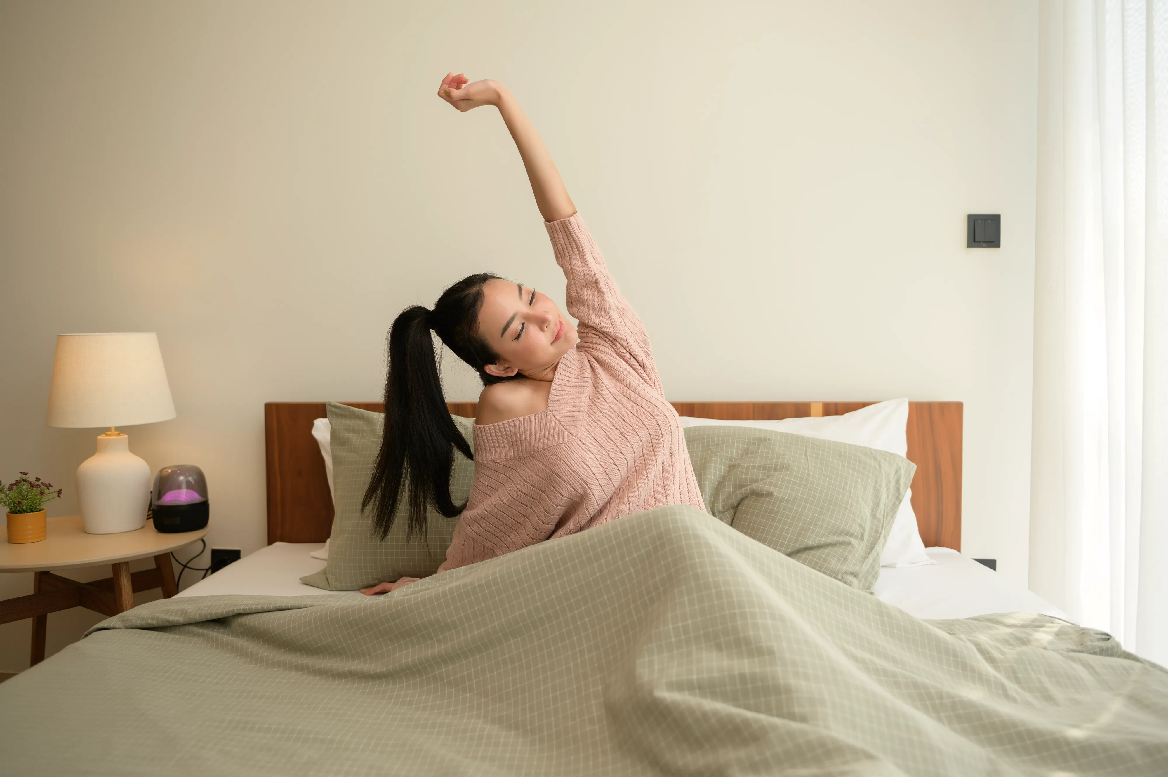 Young asian woman stretching in bed after Waking up in the Morning