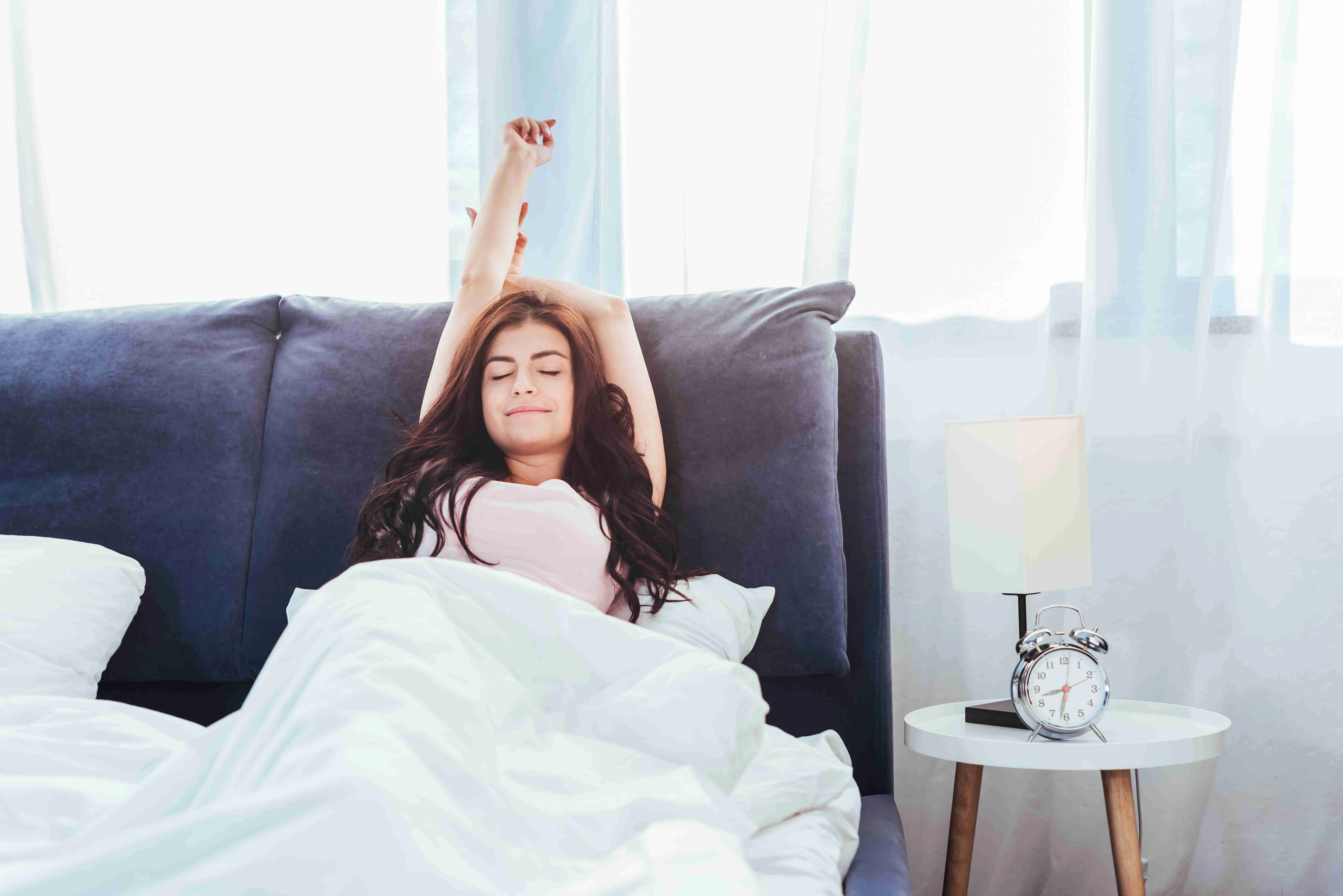 pretty young woman stretching on bed during morning time at home