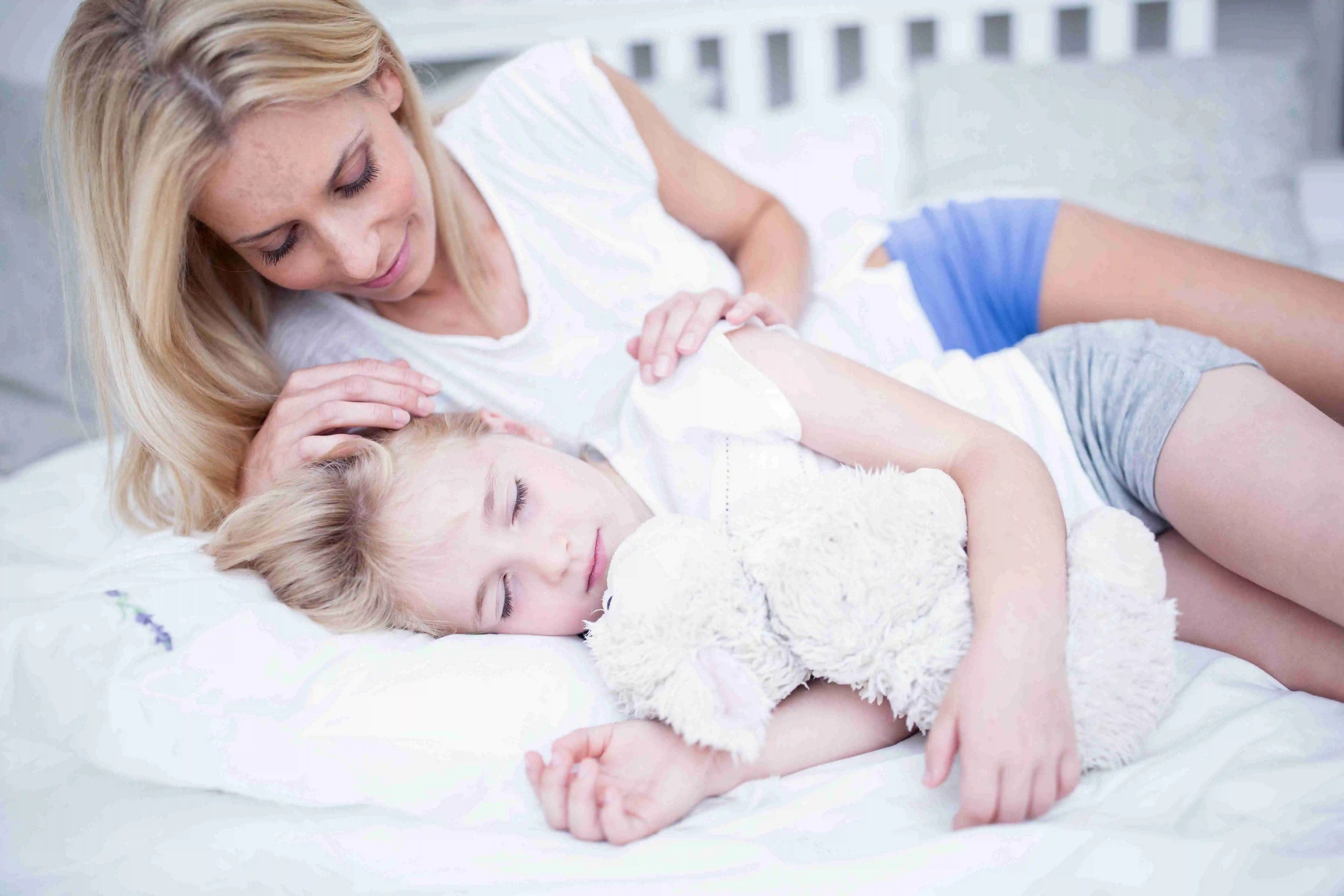 Mother looking at sleeping daughter in bed