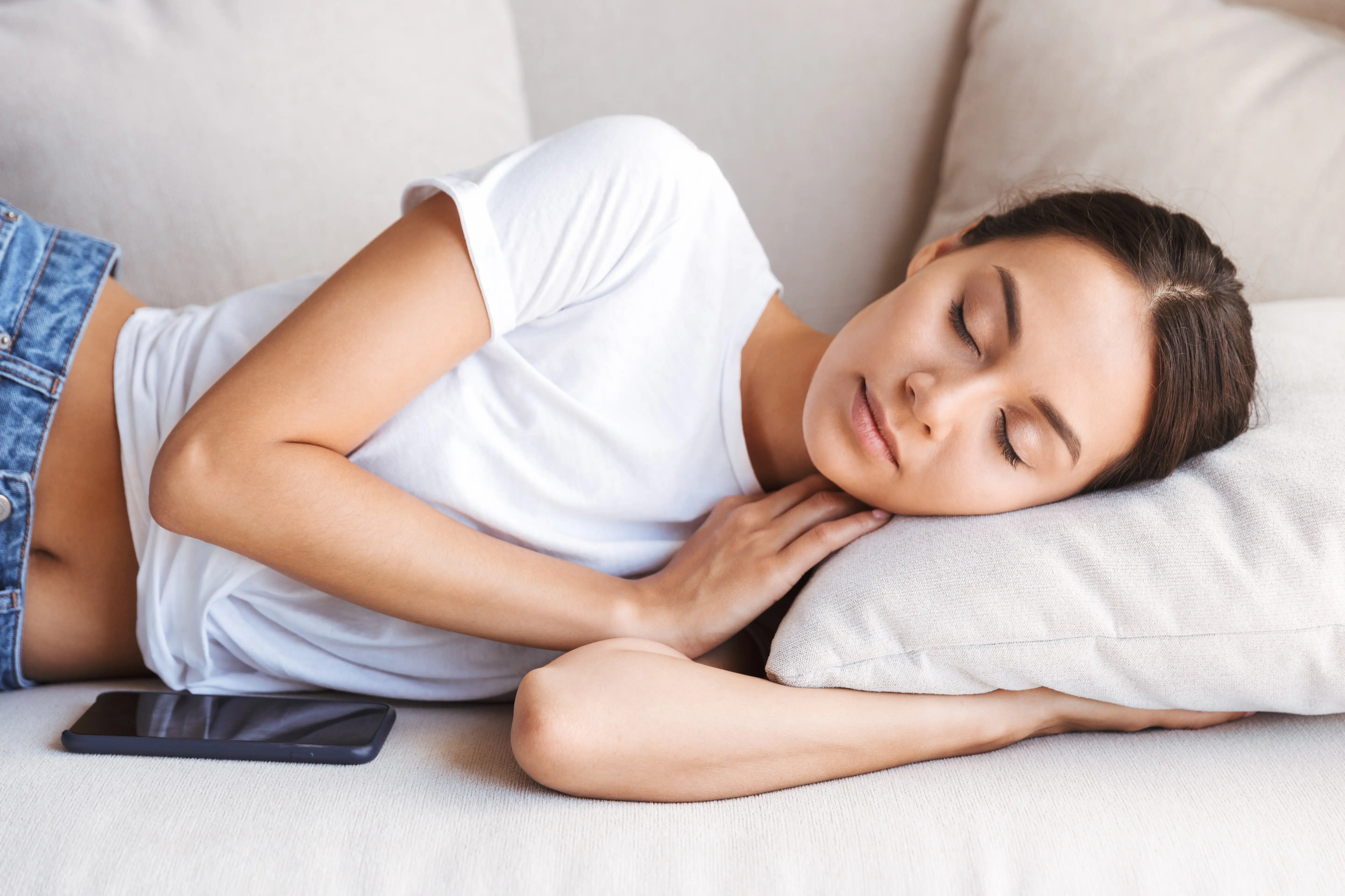 Pretty young Asian woman sleeping with mobile phone on couch at home