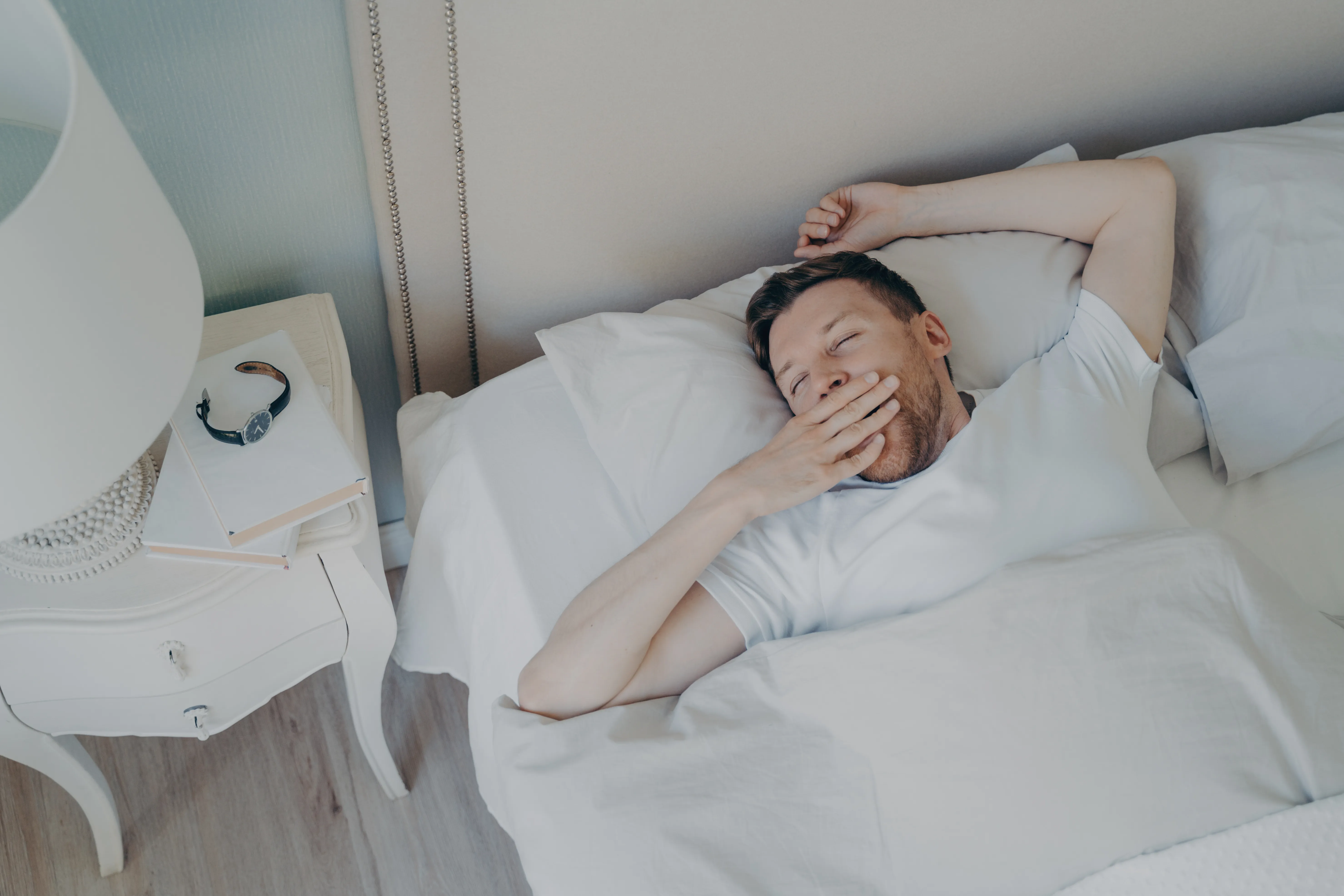 Cheerful young attractive man waking up in morning in bed